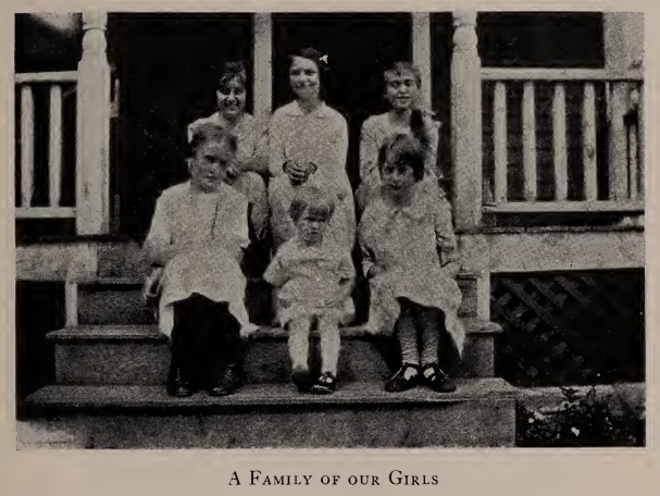 Photo of six girls and young women posed on porch steps, captioned "A Family of our Girls," from the 1923 Annual Report of the Avon Home.