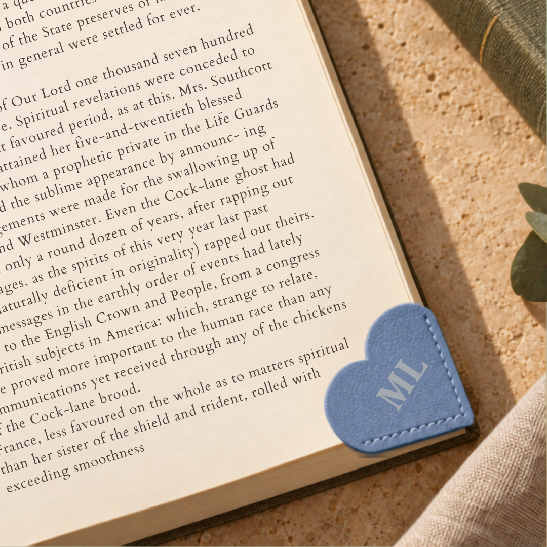 Personalised blue vegan leather heart-shaped corner bookmark on the page of an open book.