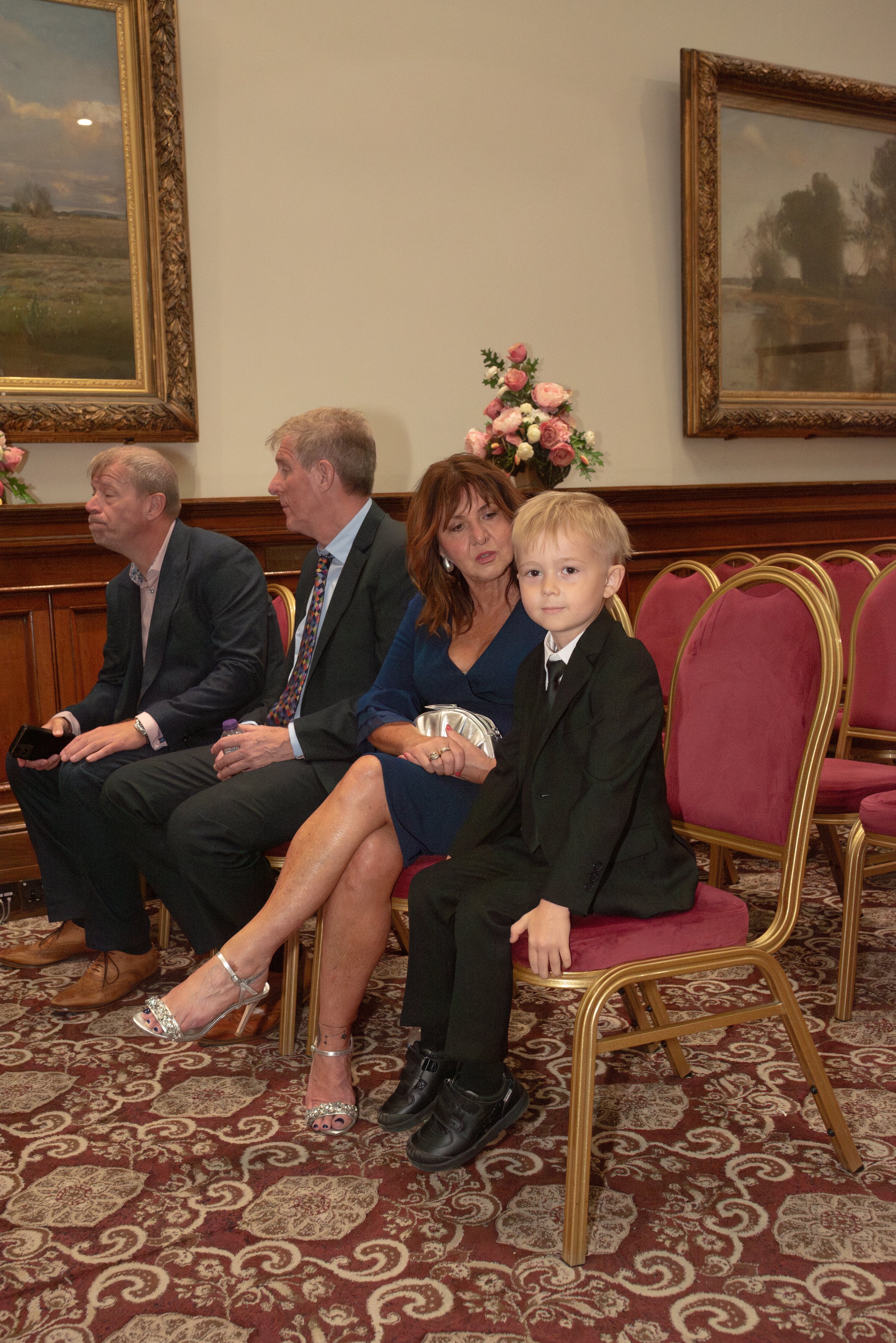 People seated in a room with pink chairs, floral paintings, and floral arrangements.