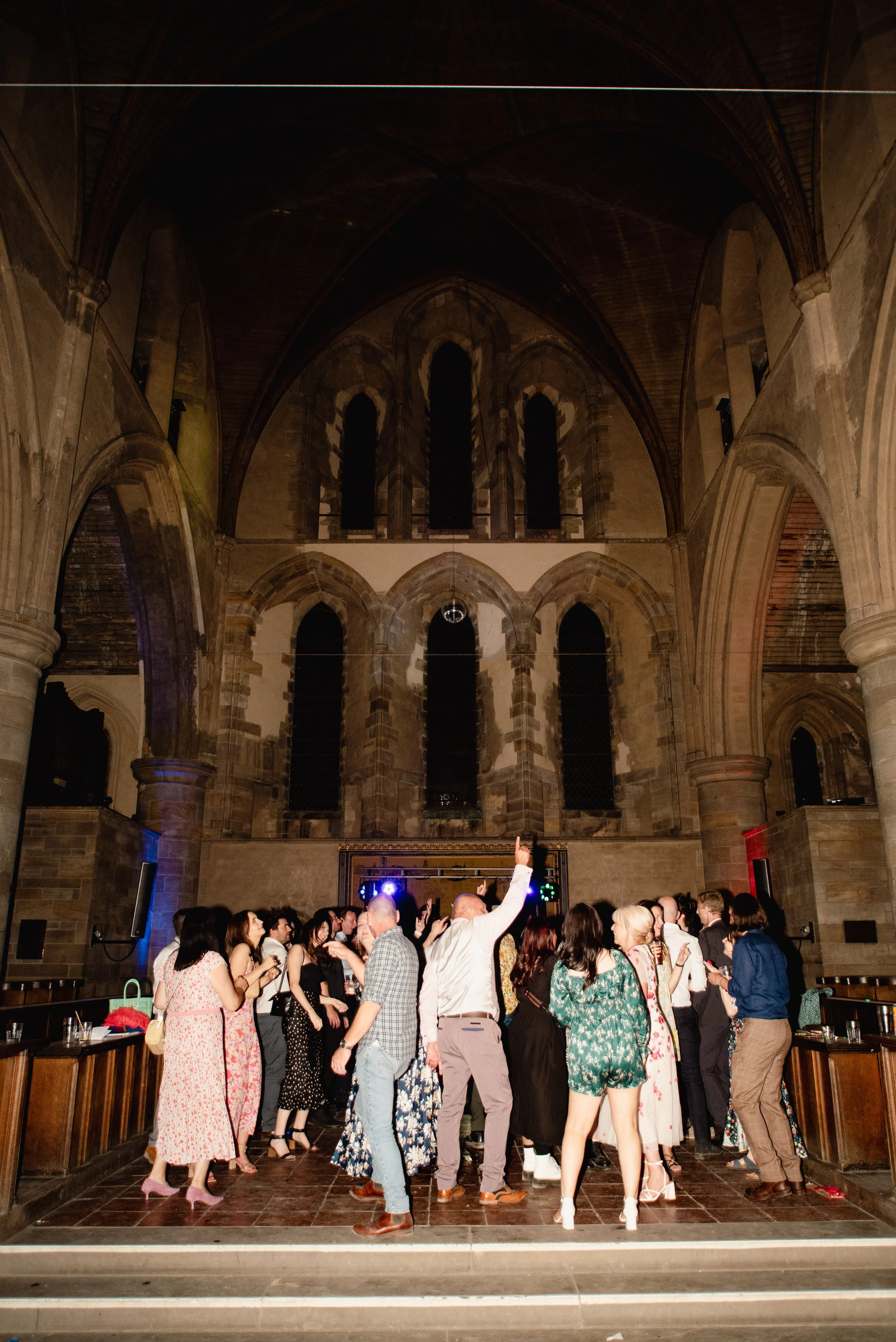 People dancing and socializing inside a church or cathedral with high vaulted ceilings and stained glass windows.