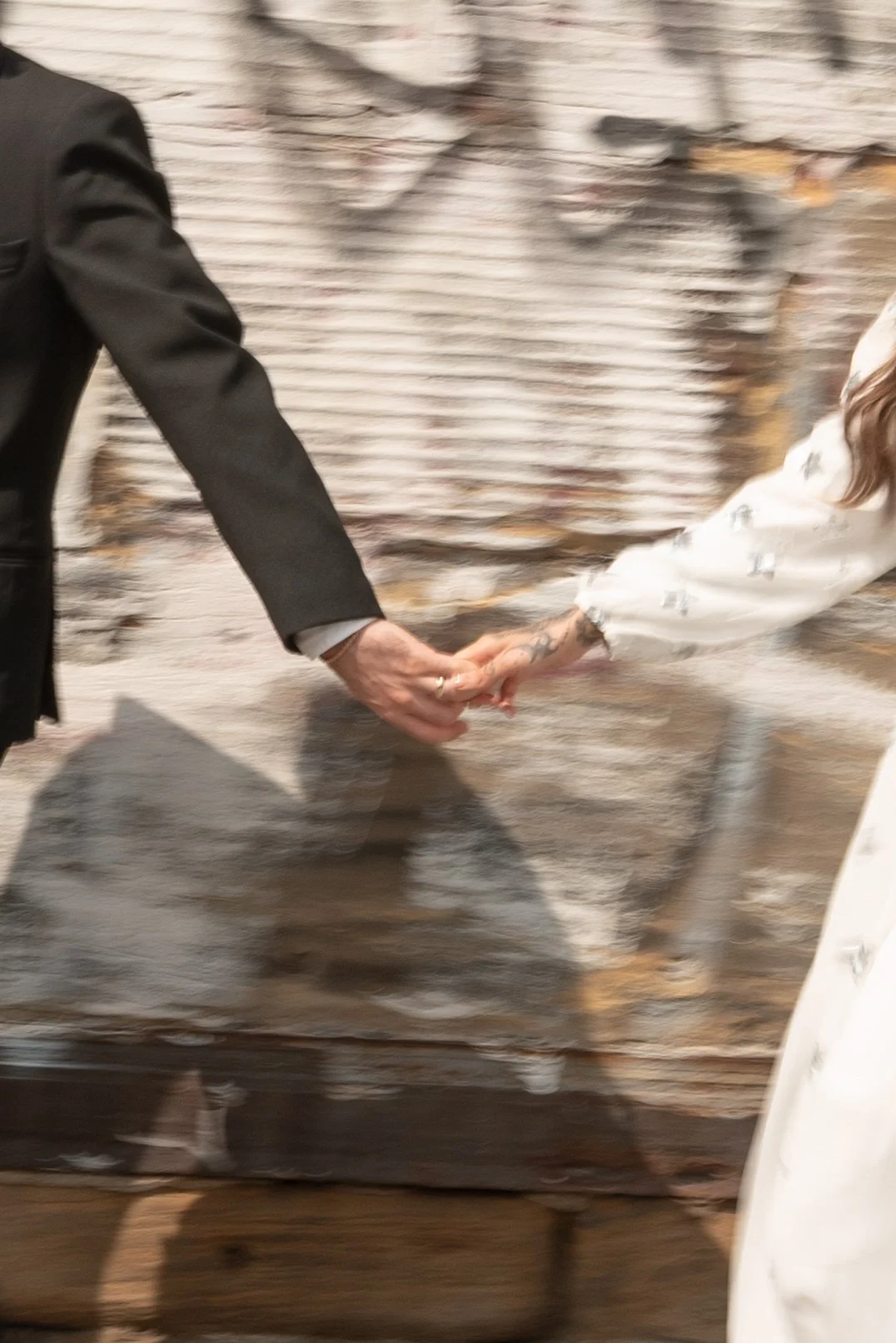 Two people are holding hands in front of a brick wall background.