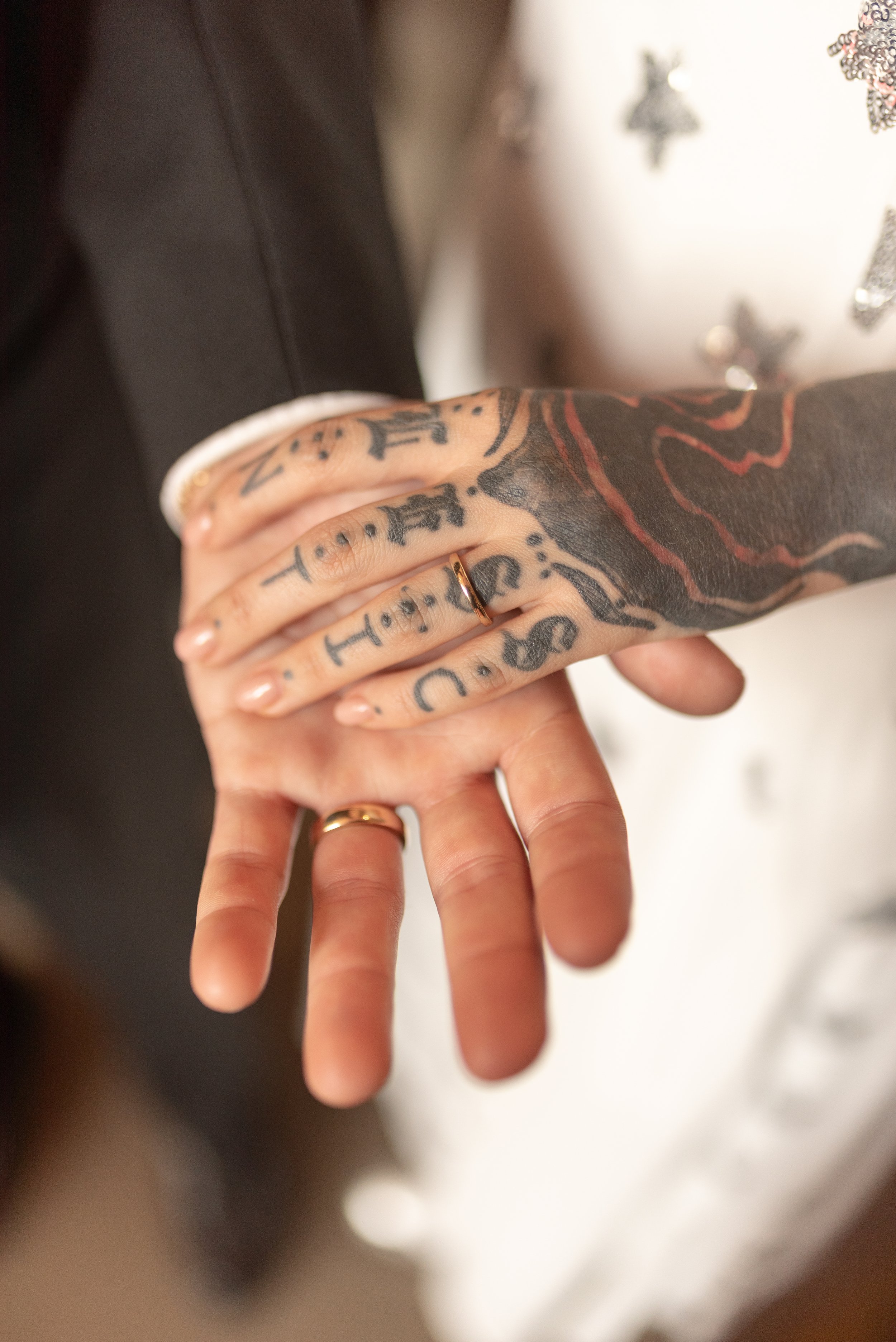 Close-up of two hands with wedding rings, one hand tattooed, holding each other.