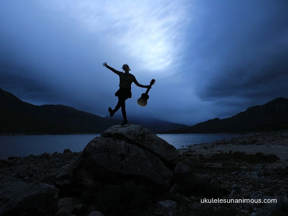 Girl with ukulele under a dark moody sky.