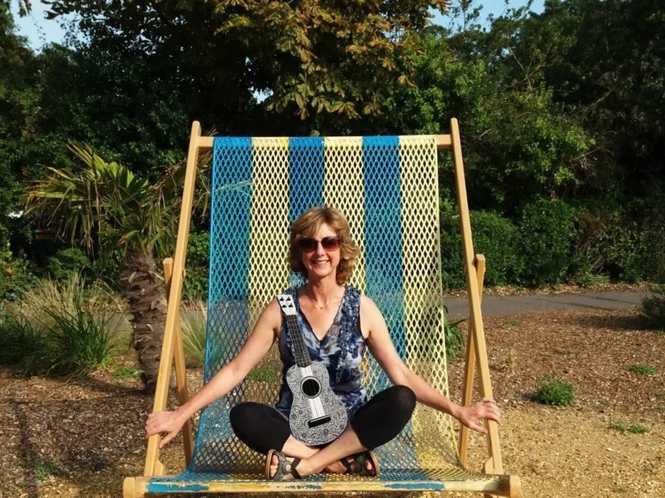 Lady sitting in an oversized deckchair with a ukulele.