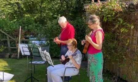 3 people playing ukulele in the garden.