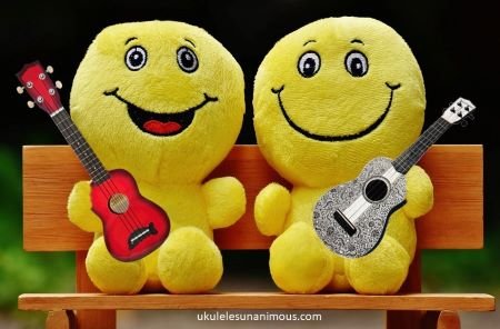 Two happy people sitting on a bench holding ukuleles.