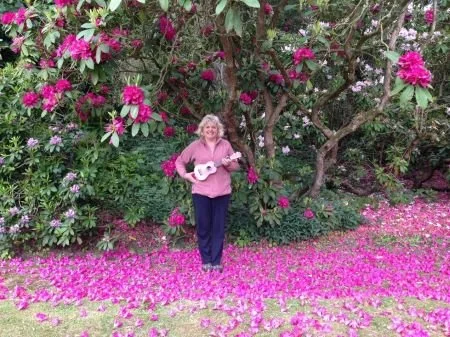 Happy lady playing pink ukulele in flower garden.
