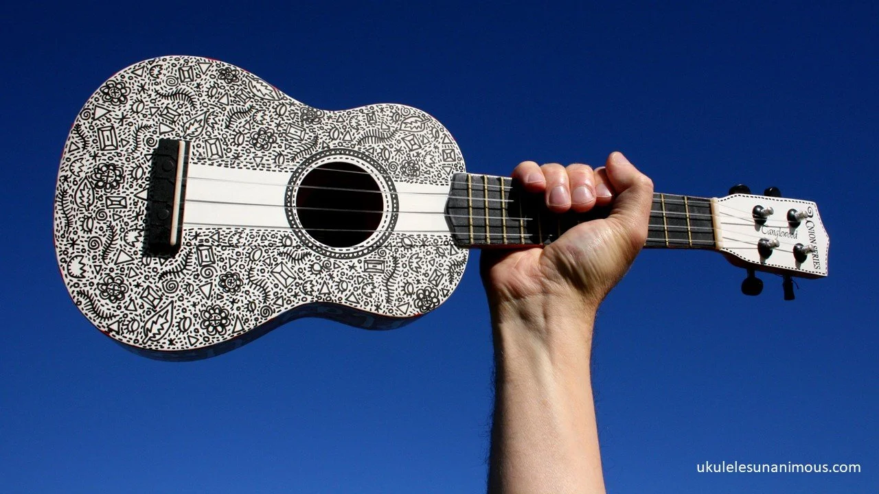 Hand holding up a white ukulele against blue sky.