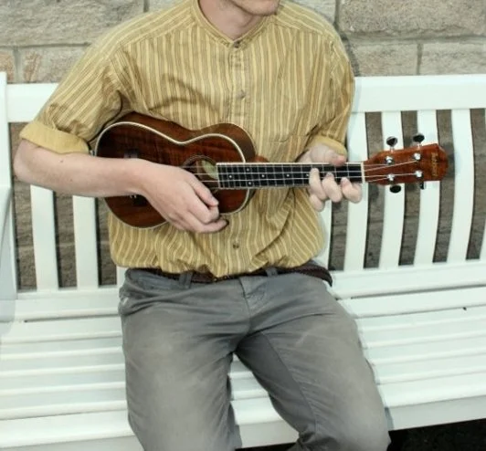 Man sitting on bench holding a ukulele.