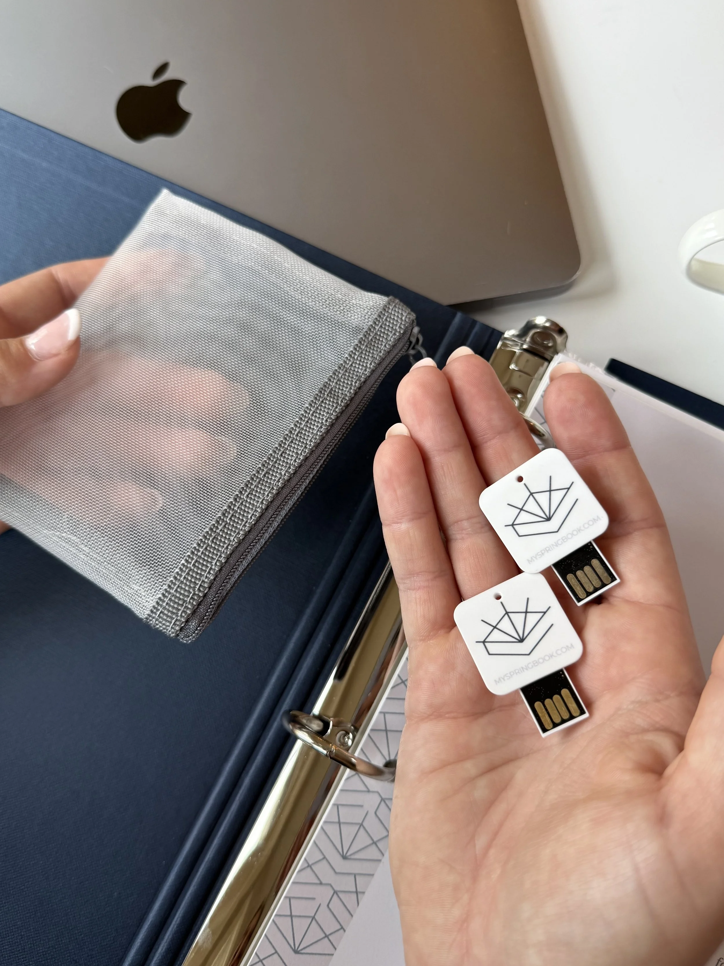 Woman holding two Springbook thumb drives with logos and a mesh grey pouch above navy blue binder