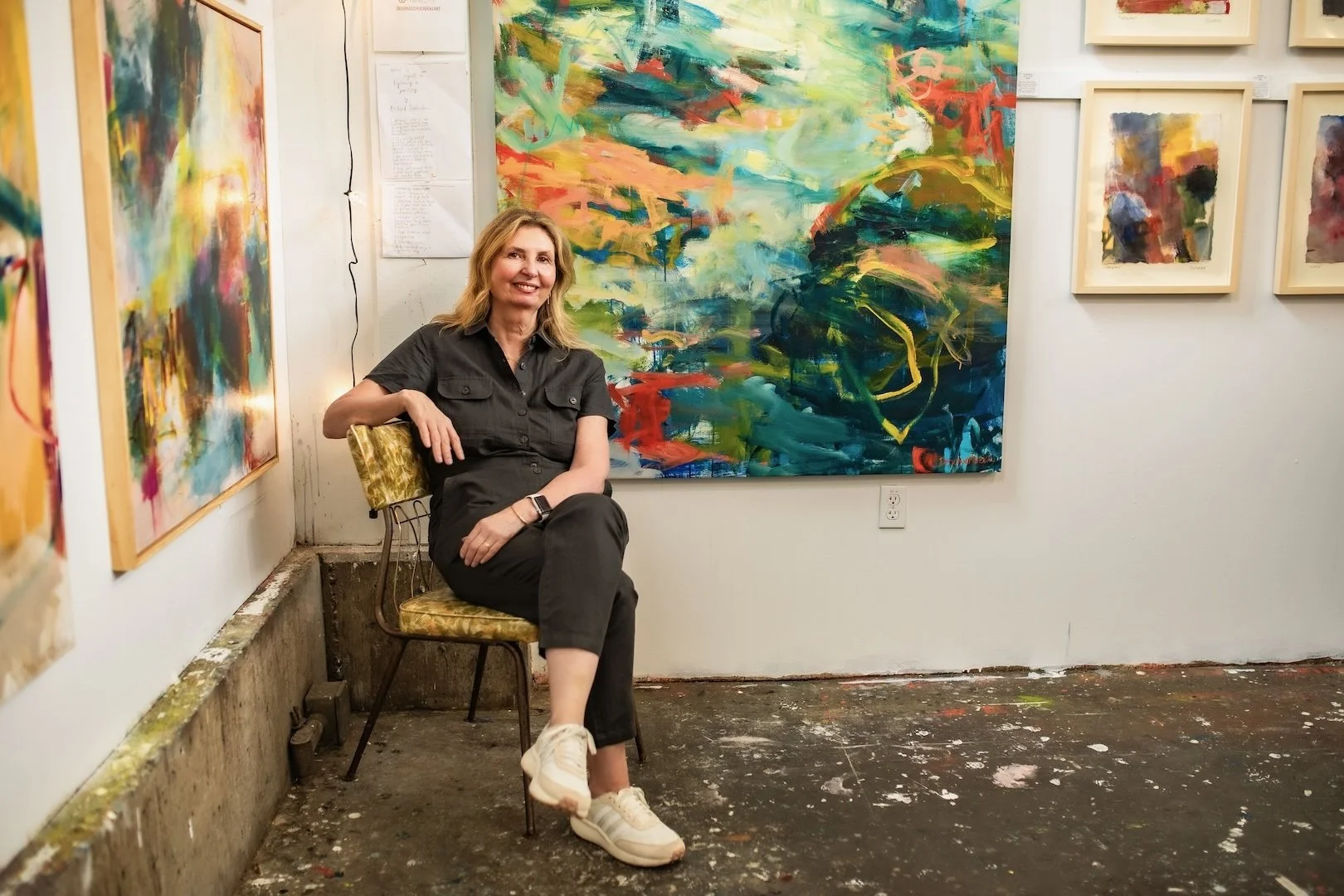 Woman sitting on a chair in an art gallery surrounded by colorful abstract paintings.