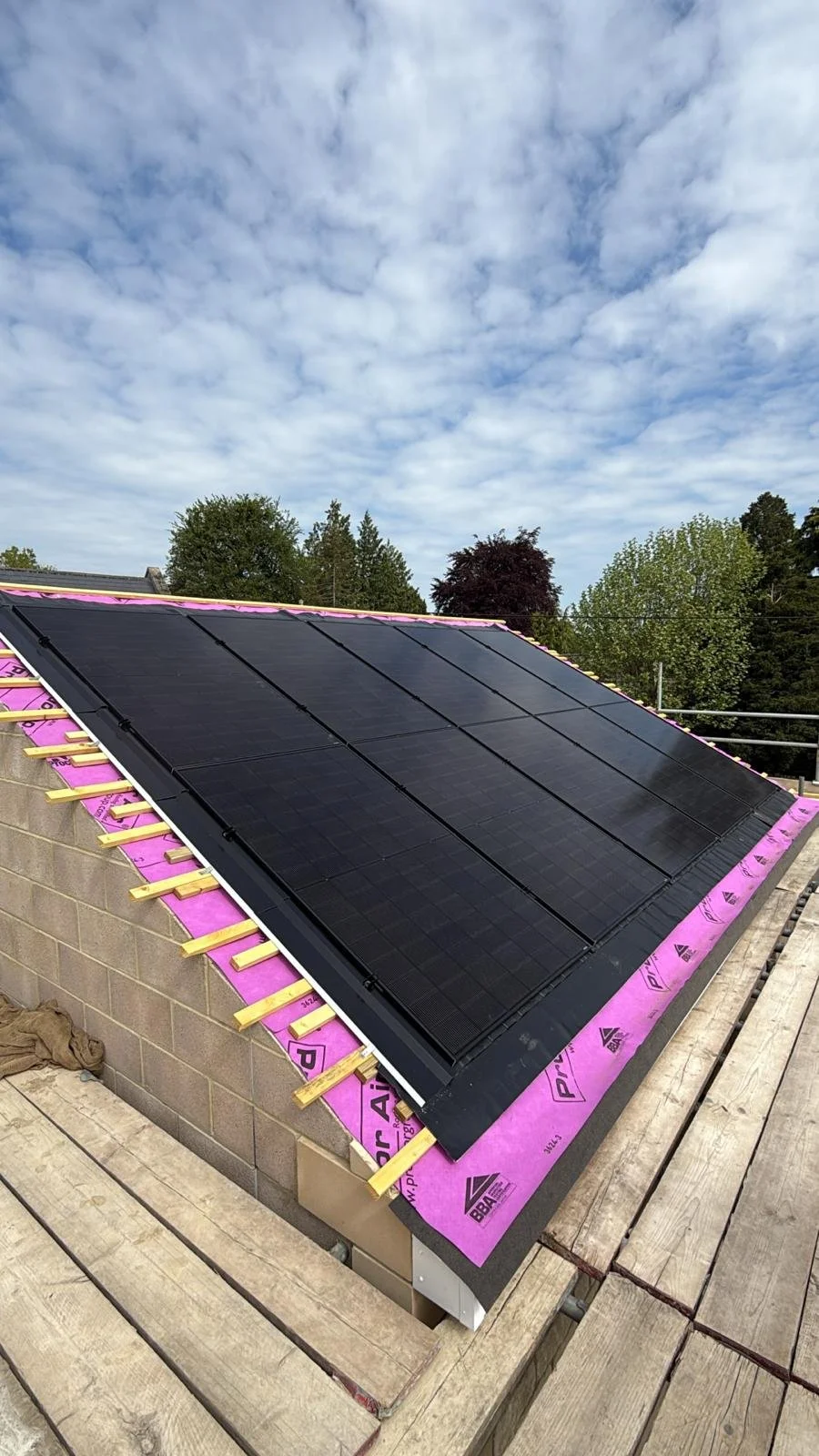 Roof with installed black solar panels under a cloudy sky, with some unfinished roofing materials visible.