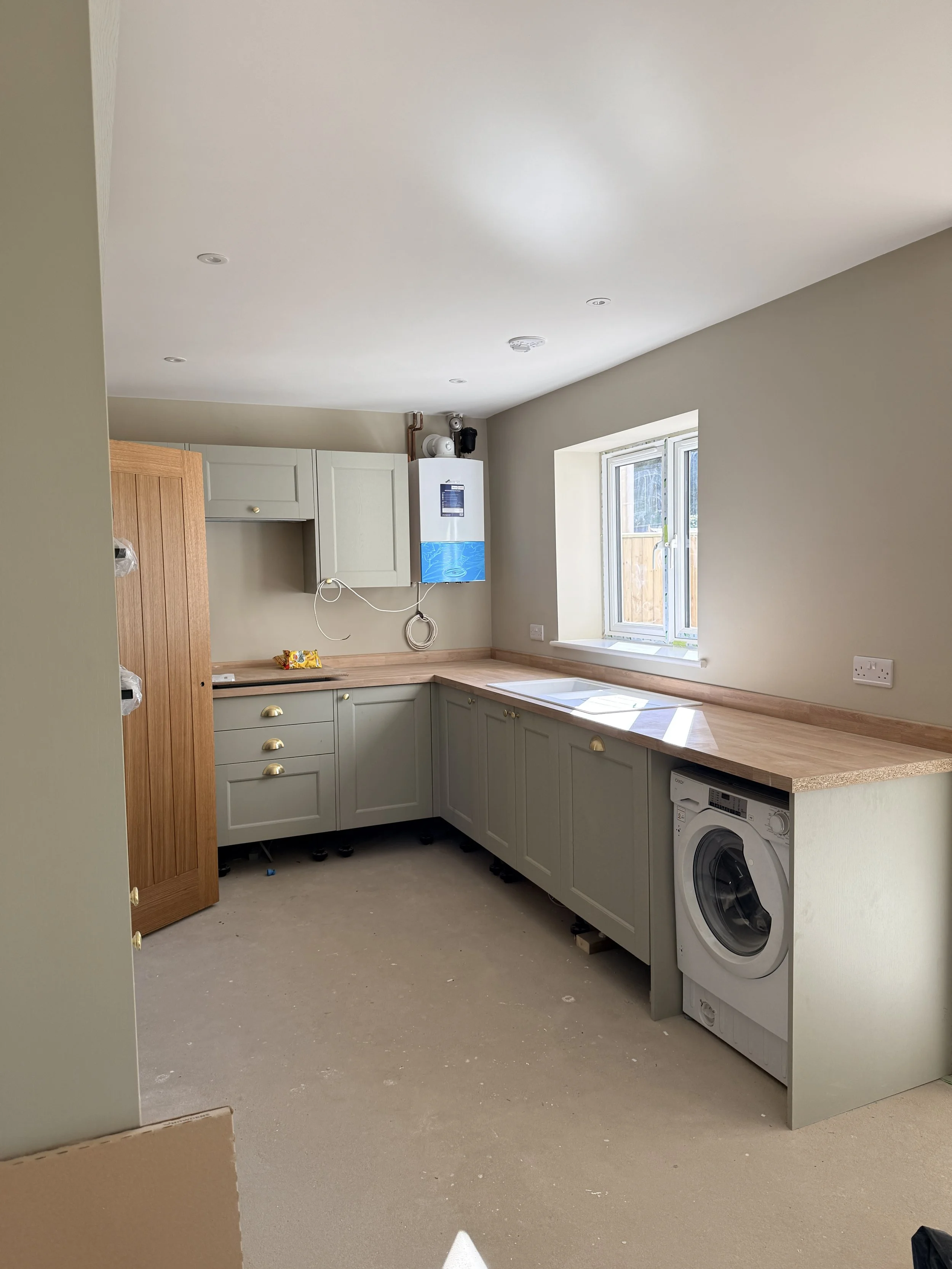 A partially finished kitchen with green cabinets, a window, and a washing machine.