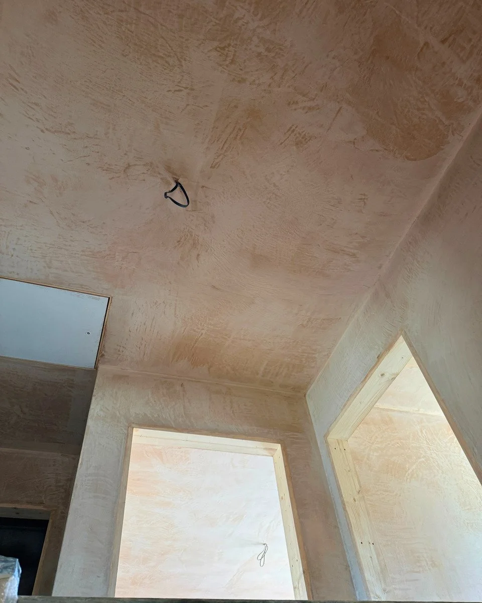 Interior view of a building under construction with unfinished drywall and openings for doors or windows, with wires hanging from the ceiling.