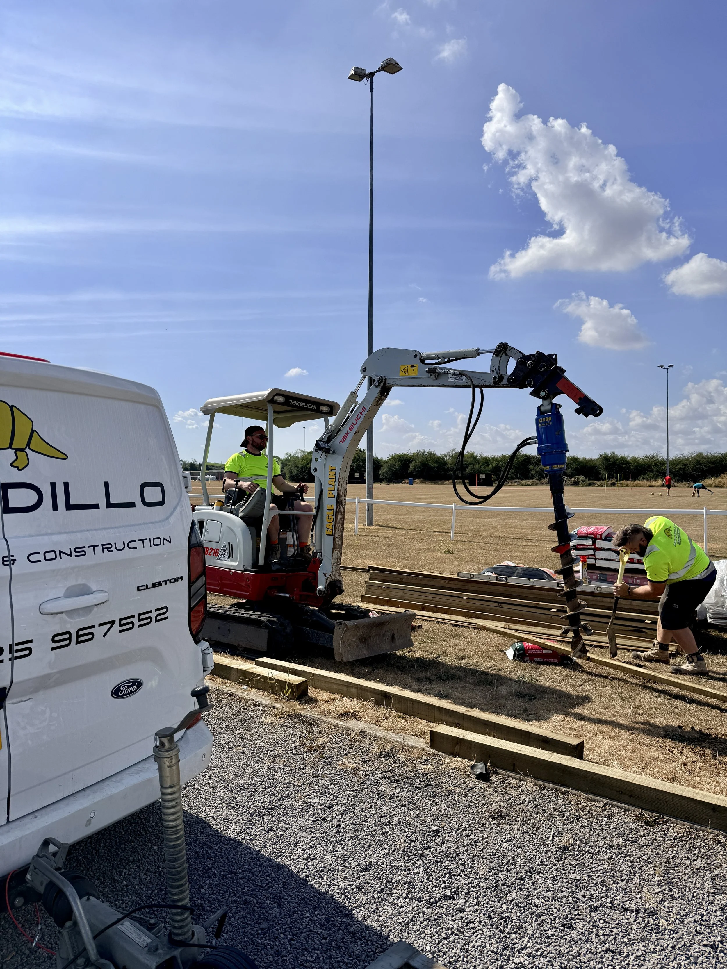 Workers installing wooden beams on a construction site with a crane and equipment, on a sunny day with few clouds.