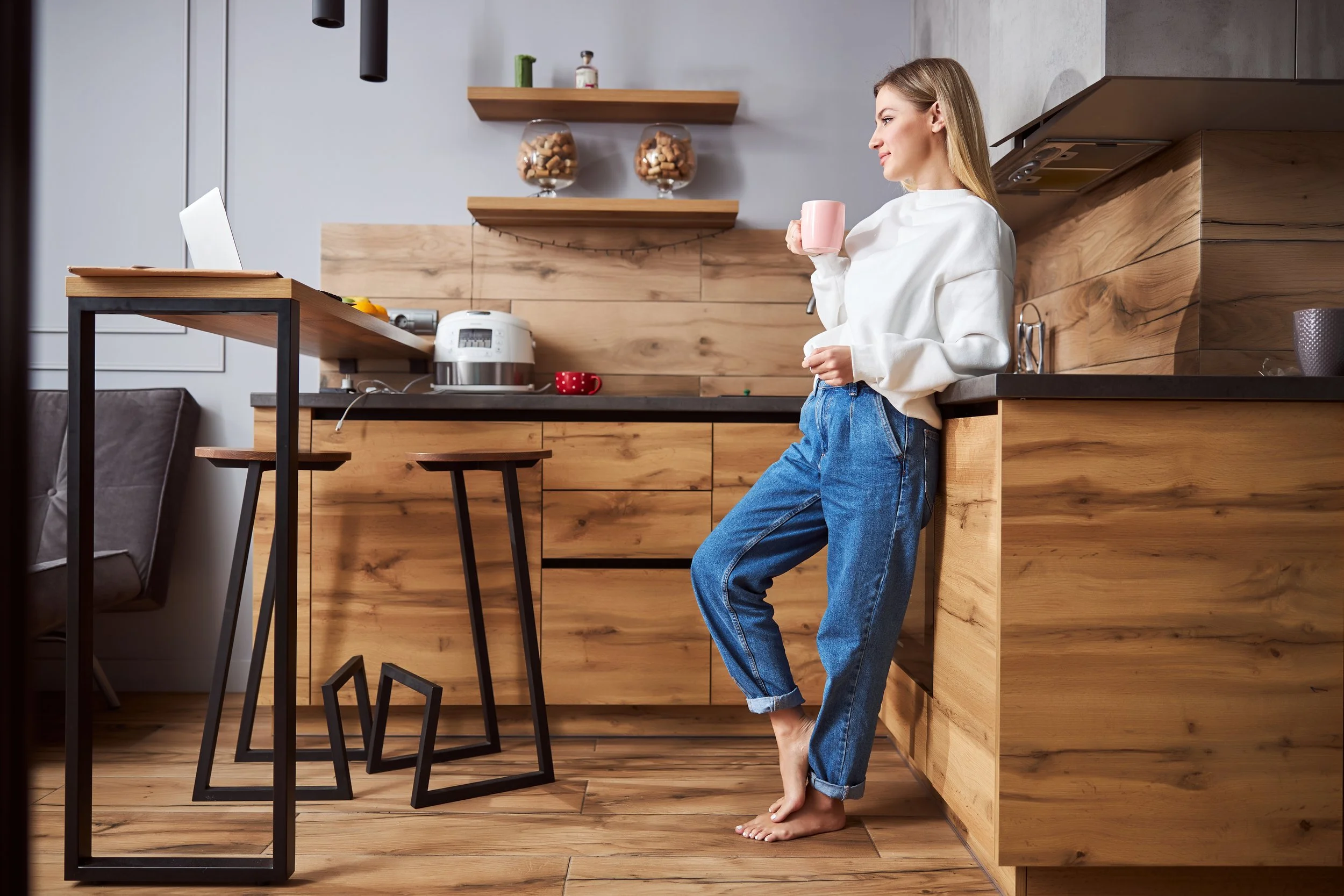  A woman stands barefoot in her kitchen sipping coffee. If you've always dreamed of having warm floors thanks to radiant floors, learn more in our comprehensive guide. 