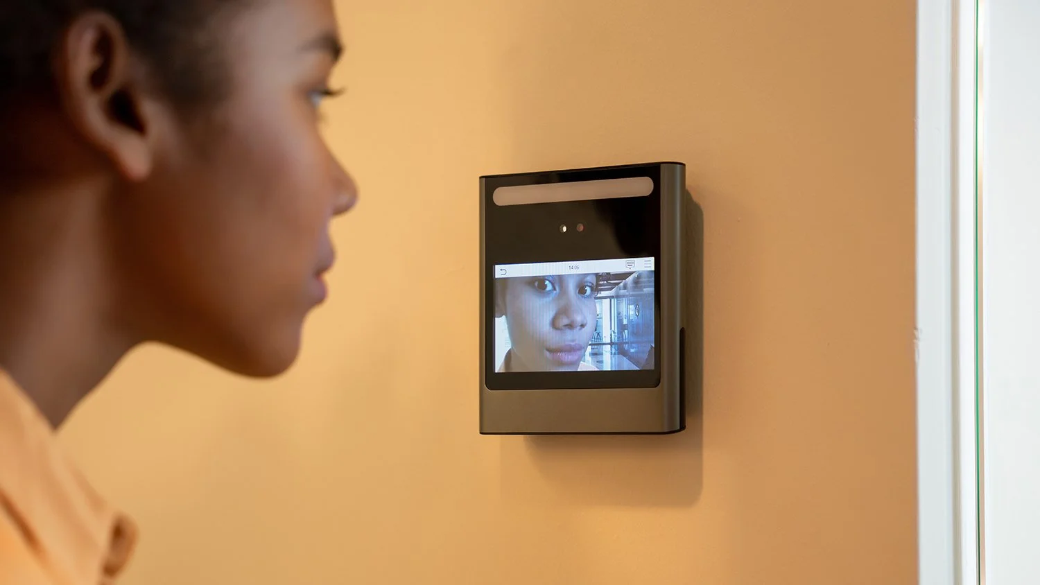  A woman uses a facial recognition device to enable her home security system. 