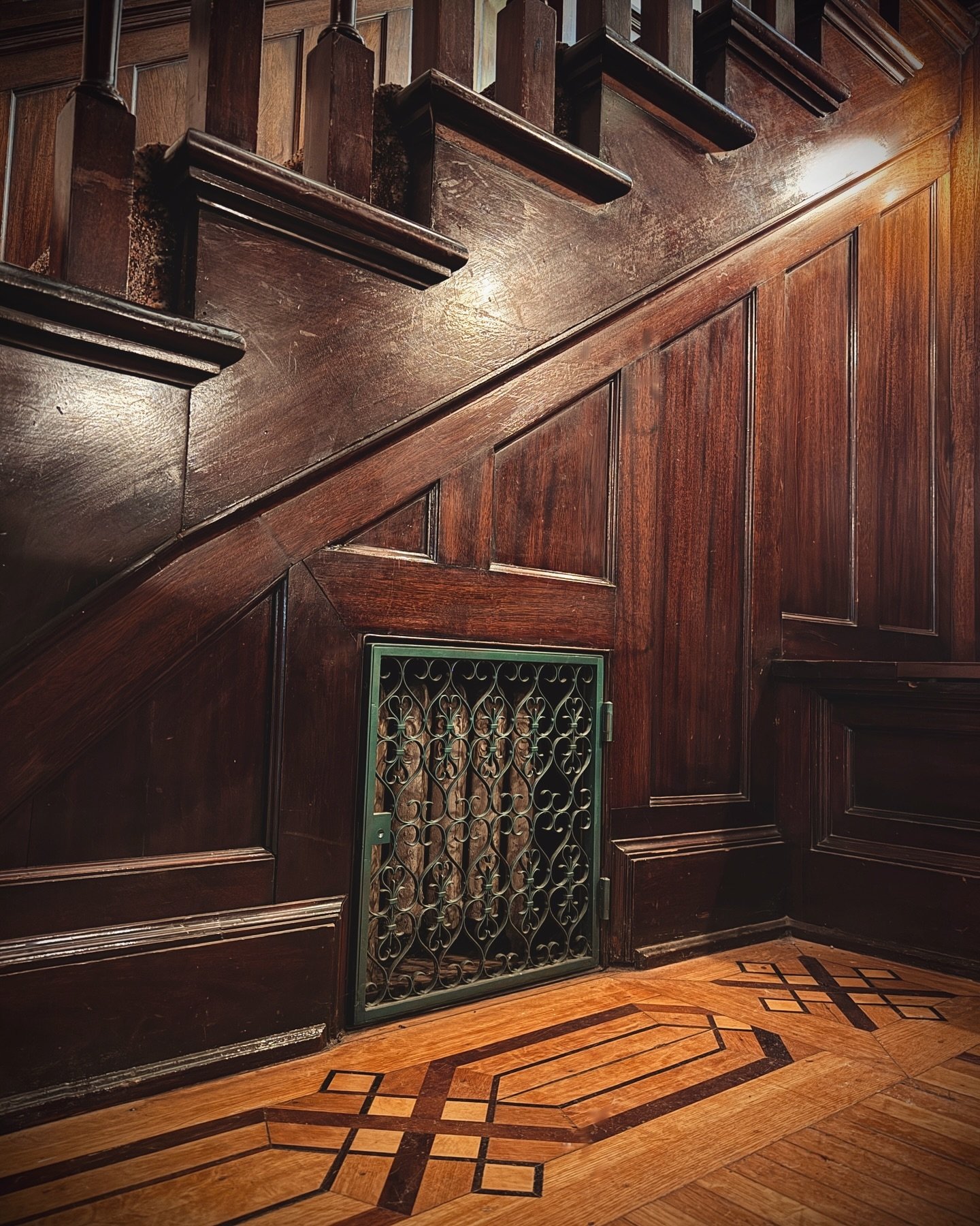 Detail of the mahogany paneling and wrought iron radiator grate cover for the built in suitors bench at the base of the stairs.