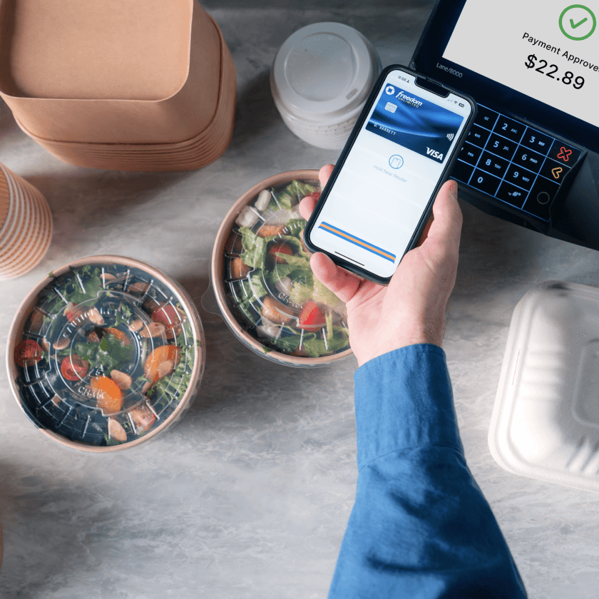 Top down photo of a hand surrounded by food, tapping their phone to pay