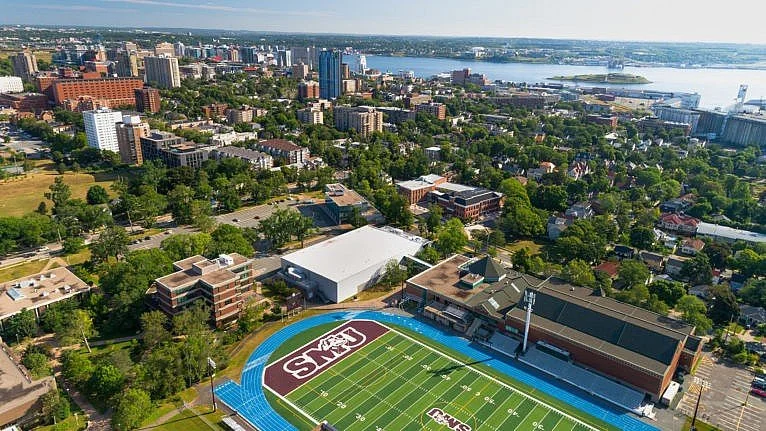 Aerial view of a university stadium with a track, a football field, and surrounding campus, set in a cityscape near a body of water.