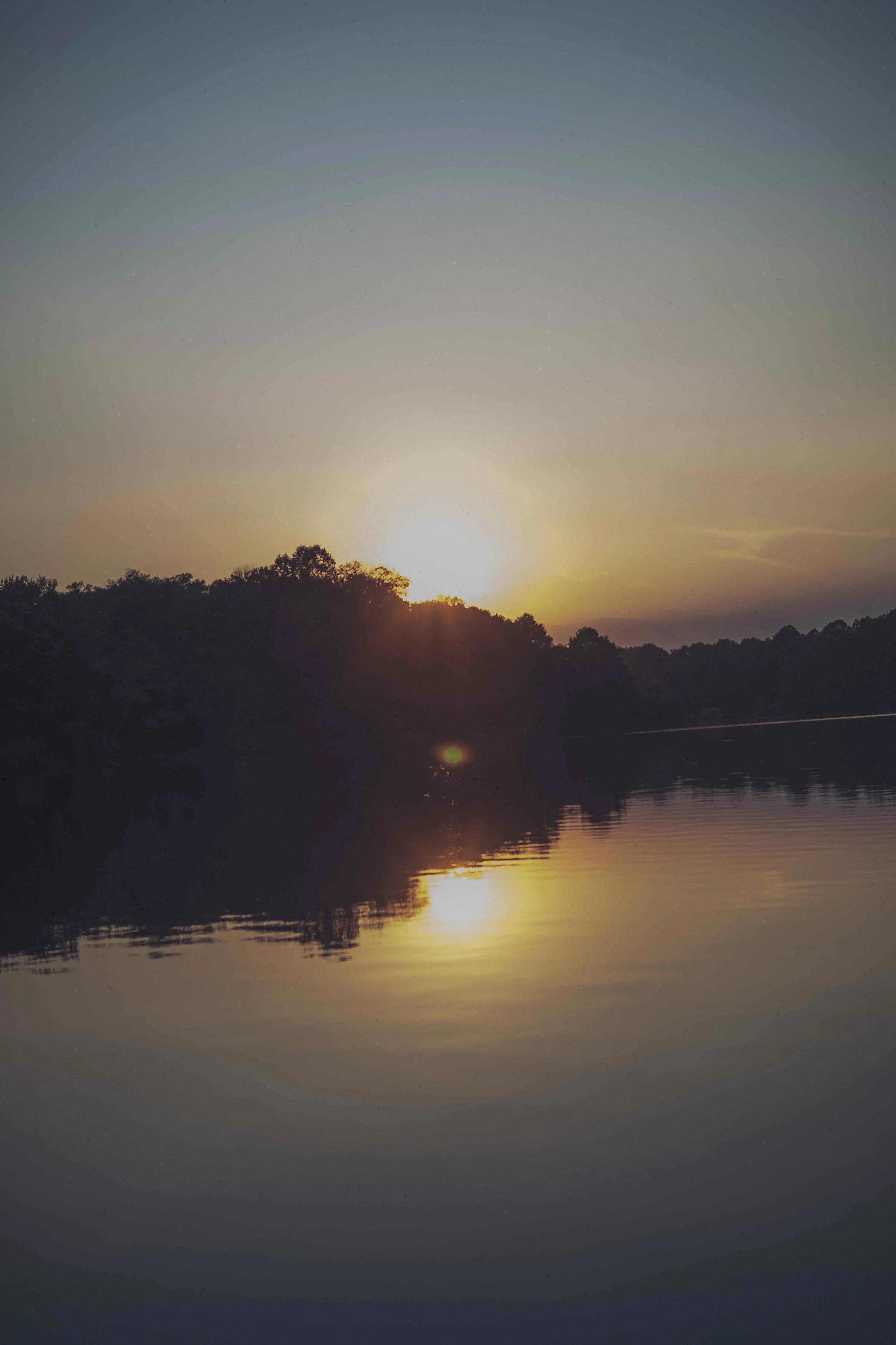 Sunset over a lake with trees on the shoreline and reflections in the water.