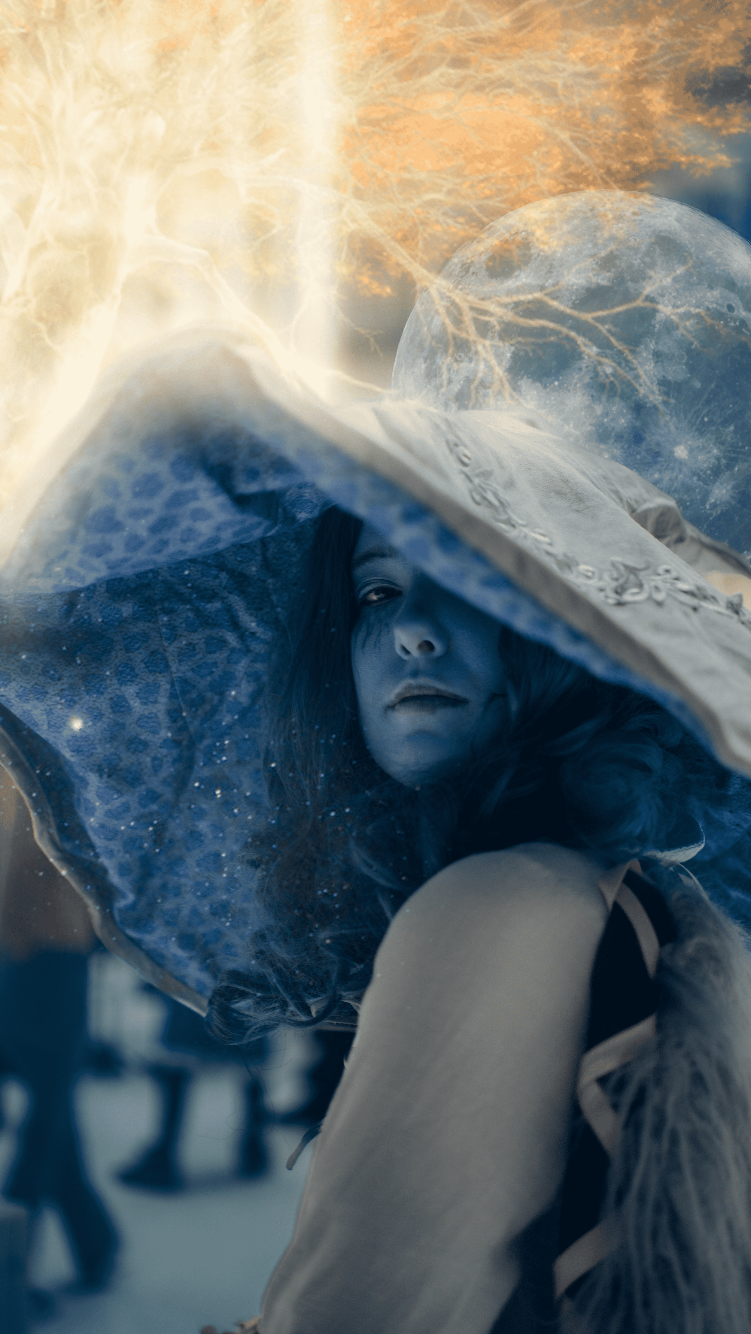 A woman with long hair and a serious expression wearing a large, semi-transparent hat with decorative elements, leaning forward against a snowy background with a full moon and orange clouds in the sky.