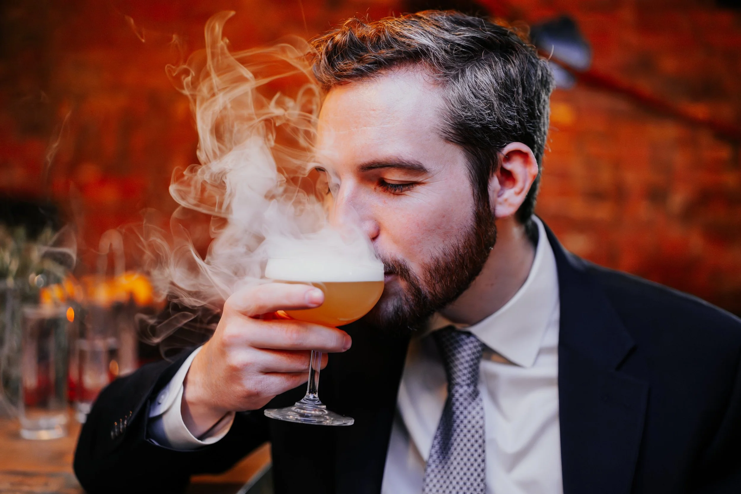 Man in suit drinking a cocktail with vapor or smoke rising from it.