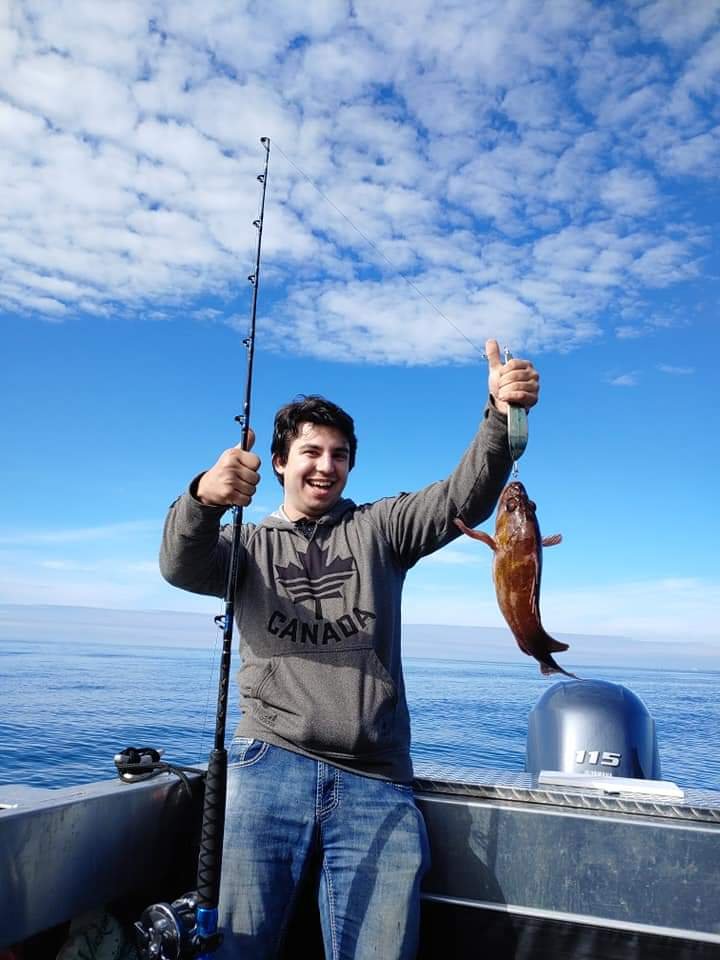 Person on a boat holding a fishing rod with a fish, ocean and blue sky in the background.