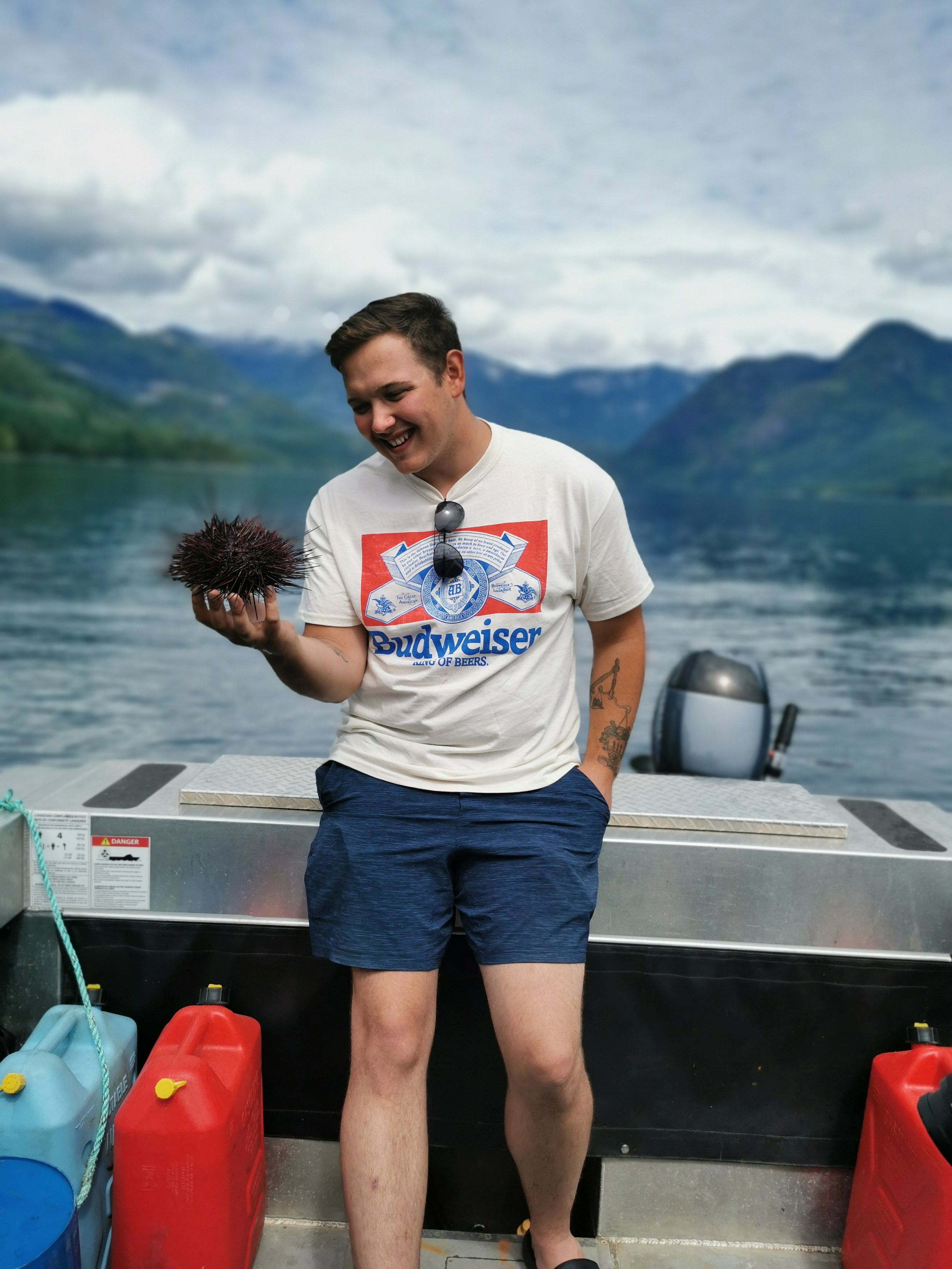 Person on boat holding a sea urchin with a mountainous lake backdrop.