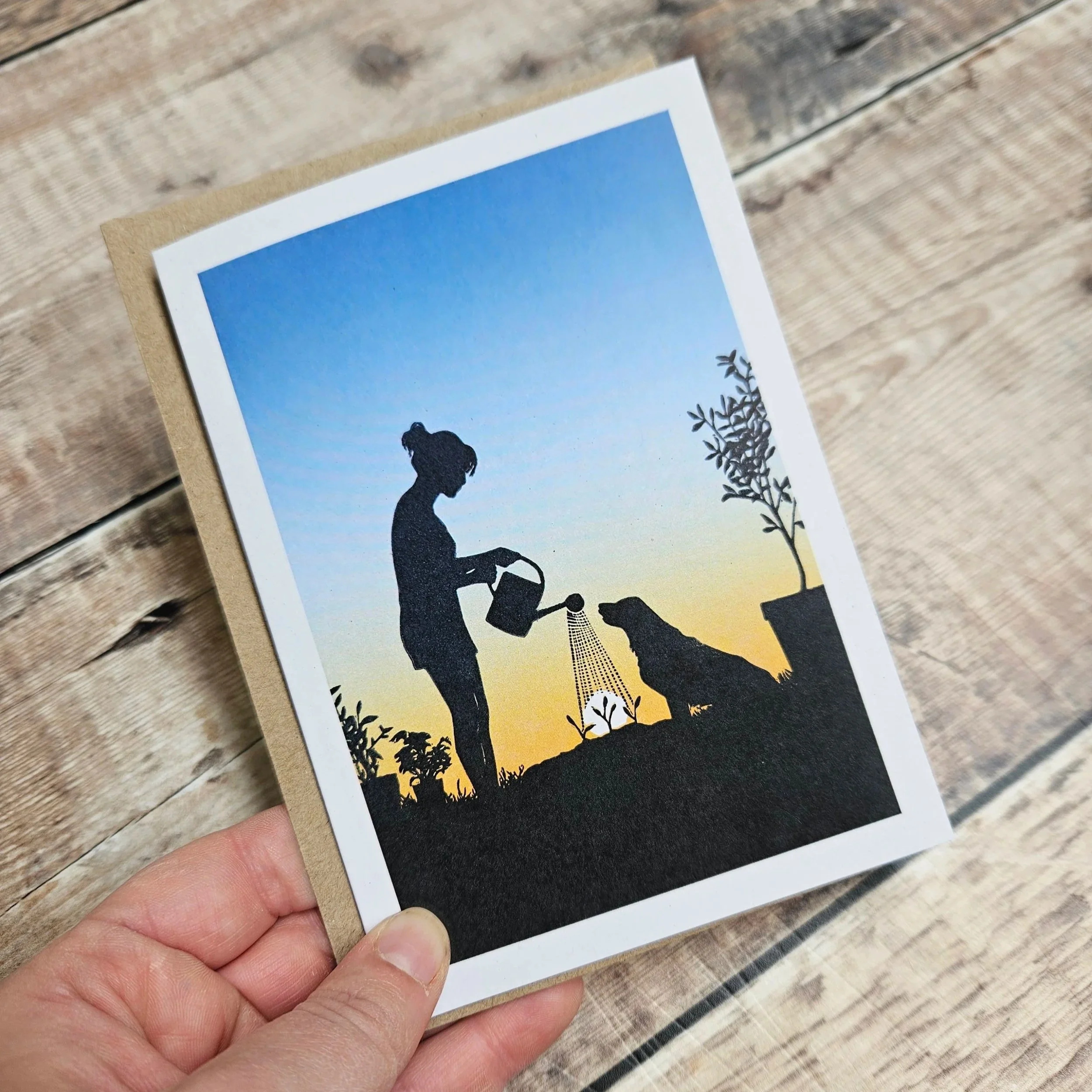Silhouette of a woman watering a seedling with her dog outdoors during sunset.