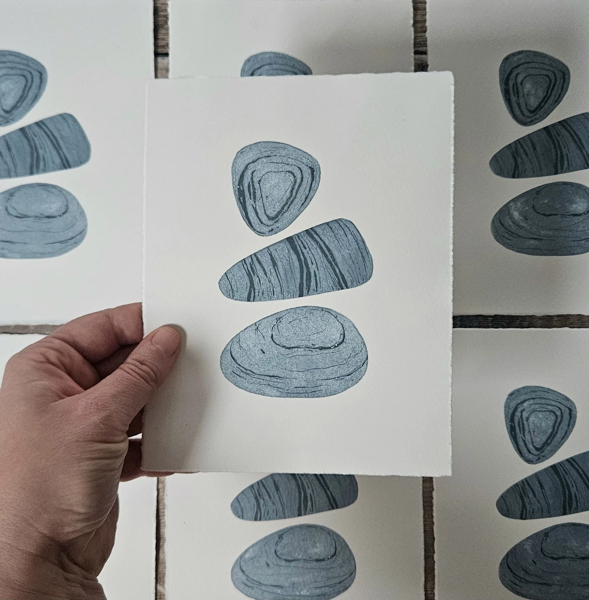 A hand holding a remnant print featuring three pebbles by the artist megan hall