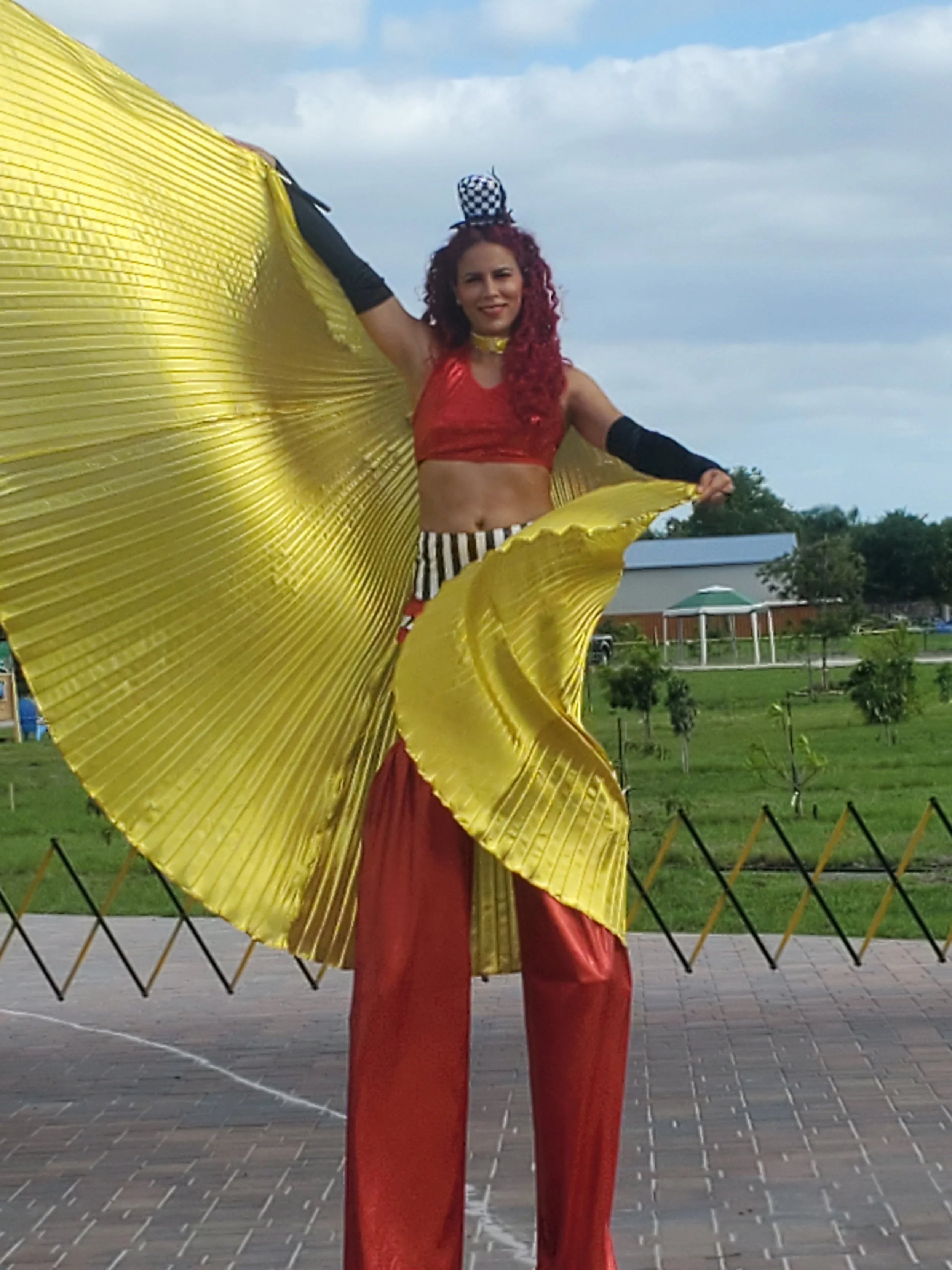 Stilt-walking at the entrance of an event wearing black and white shorts, red sequin cropped top with black gloves , shimmering red stilt-covers, golden butterfly wings, and black and white striped mini top hat headband.