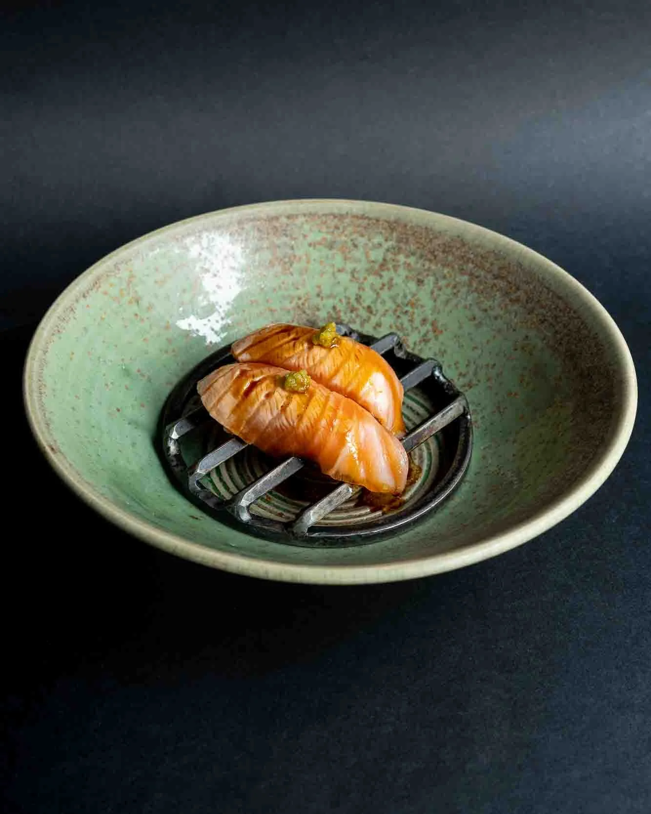 To skiver laks placeret på en stålrist i en grøn skål mod en sort baggrund.