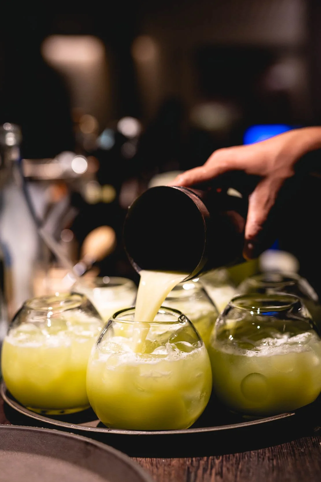 En person hælder en grøn juice i glas på en restaurant eller bar.