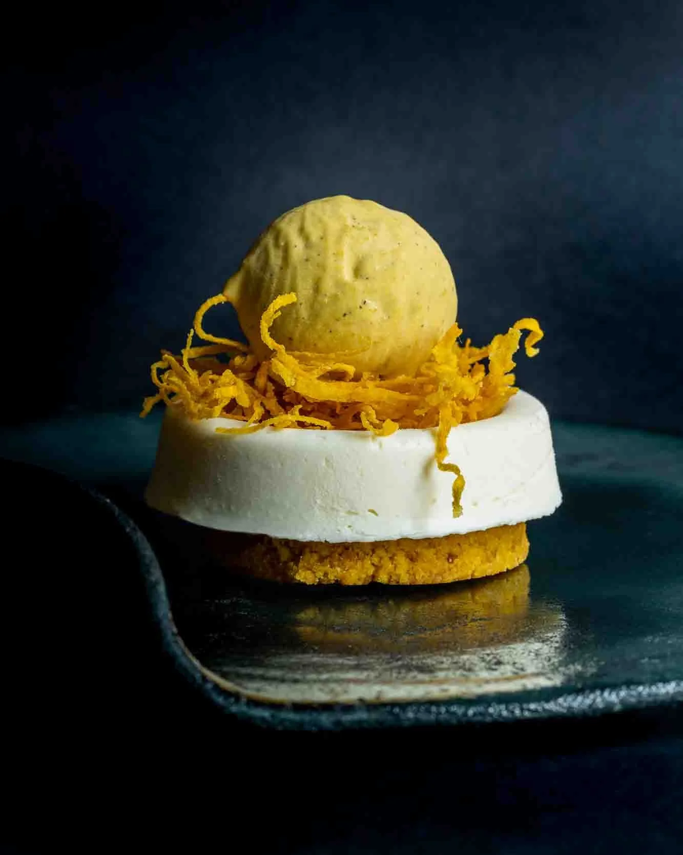 En elegant dessert med en cookie, en skive flødeost, cheddarost og en kastanie på toppen, præsenteret på en sort skænk.