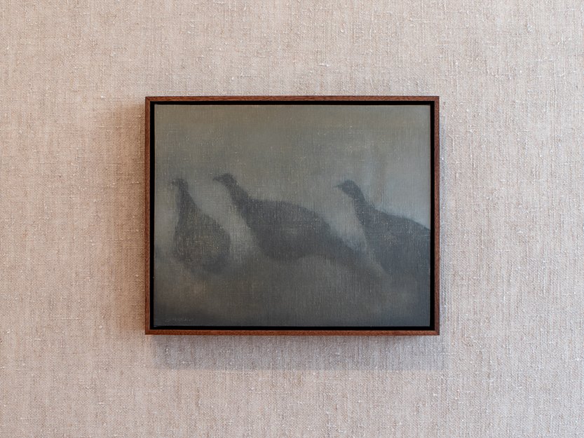 Framed oil painting of three turkeys hanging on a linen wall in a gallery room.