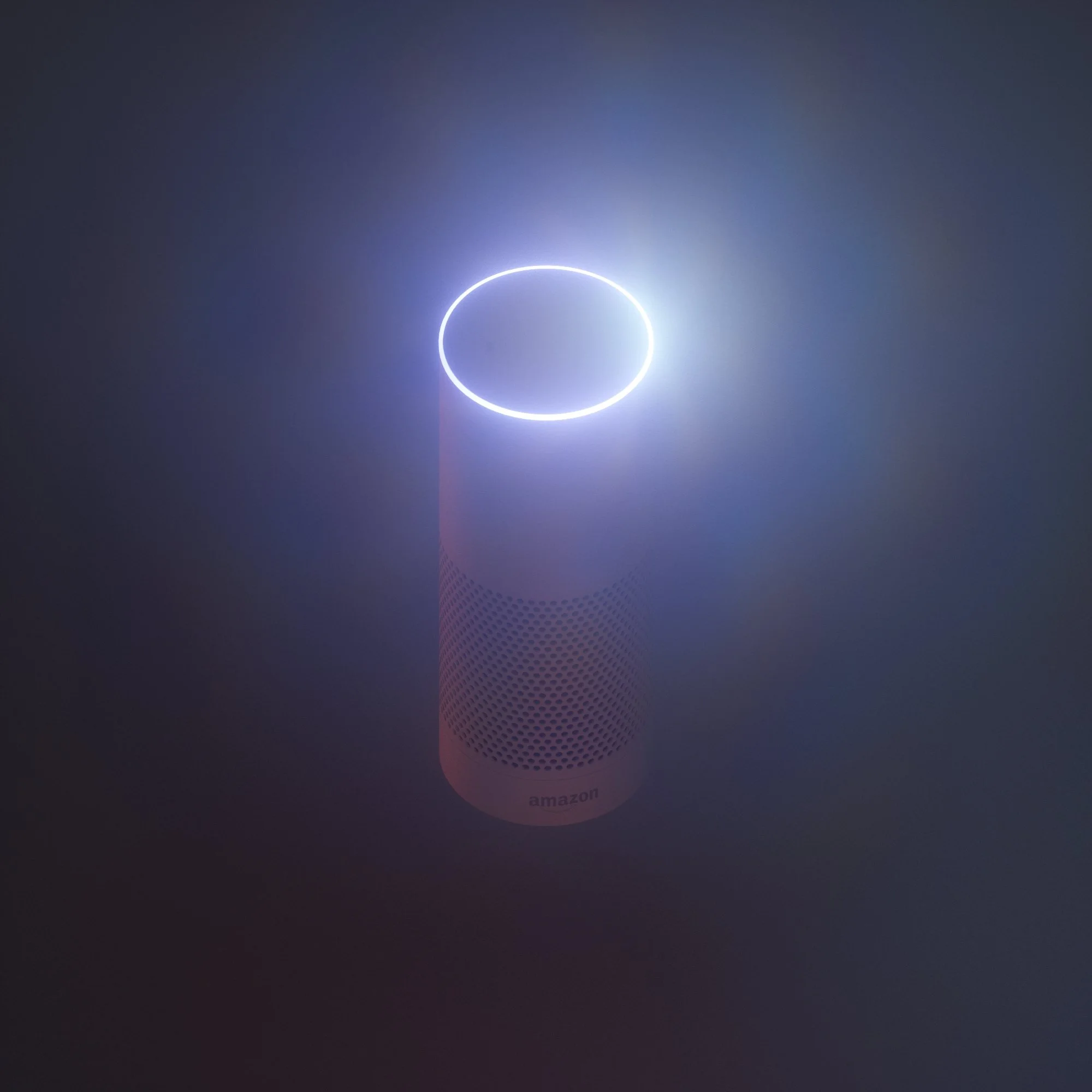 Amazon Echo smart speaker with glowing blue light in a dark room