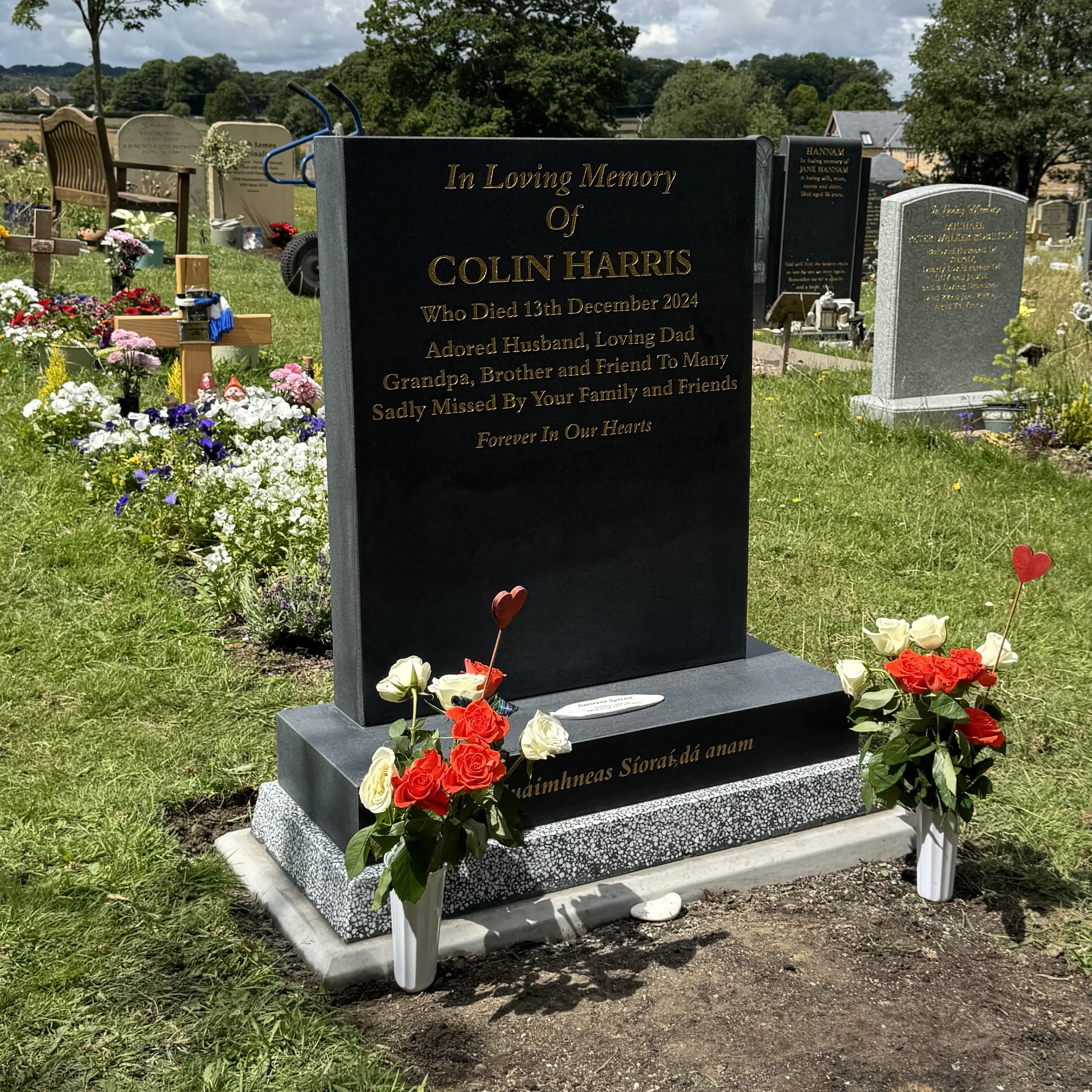 Gravestone with flowers and remembrance plaques in a cemetery, dedicated to Colin Harris who died December 13th, 2024.