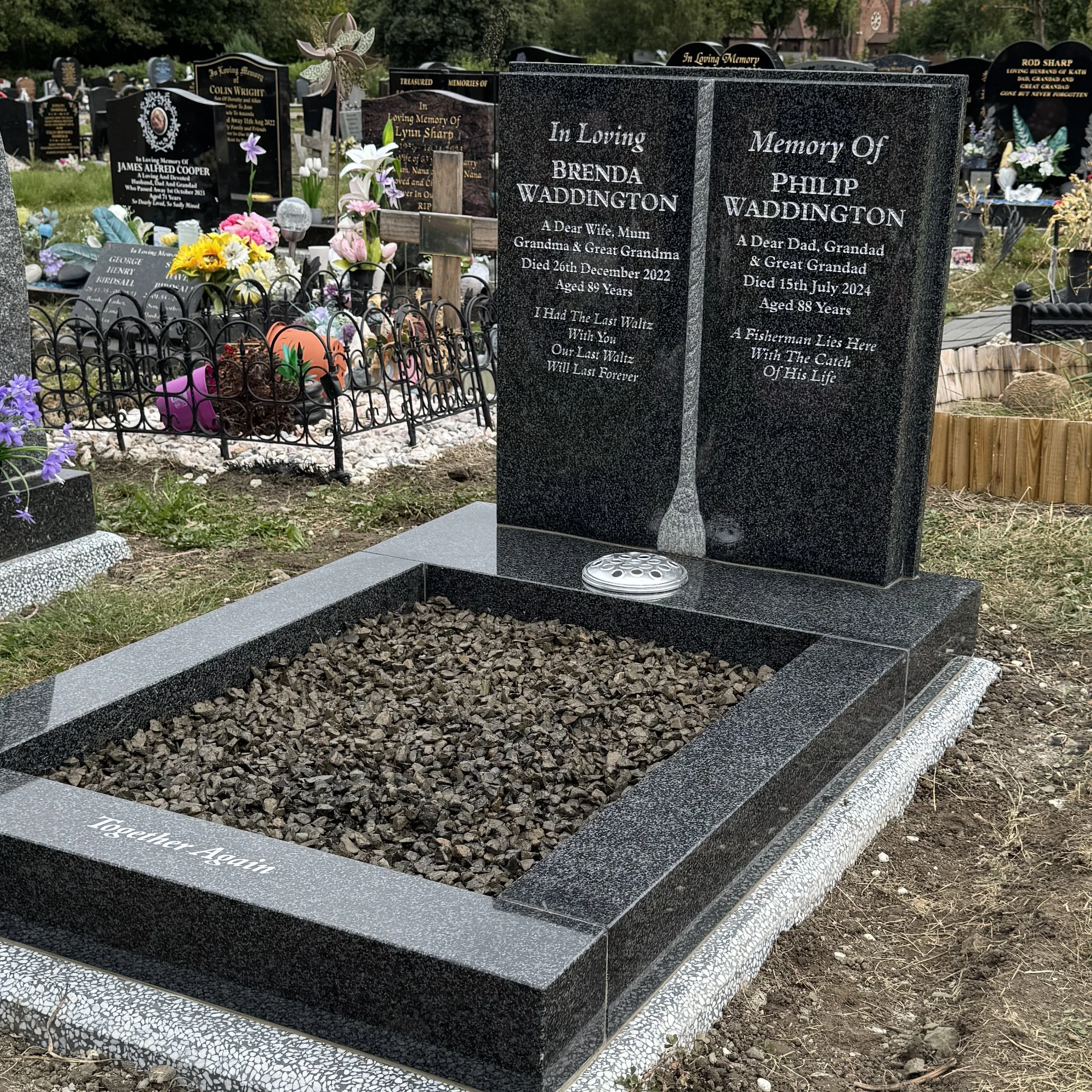Gravestone honoring Brenda and Philip Waddington with engraved poem, surrounded by colorful flowers and other graves in the background.