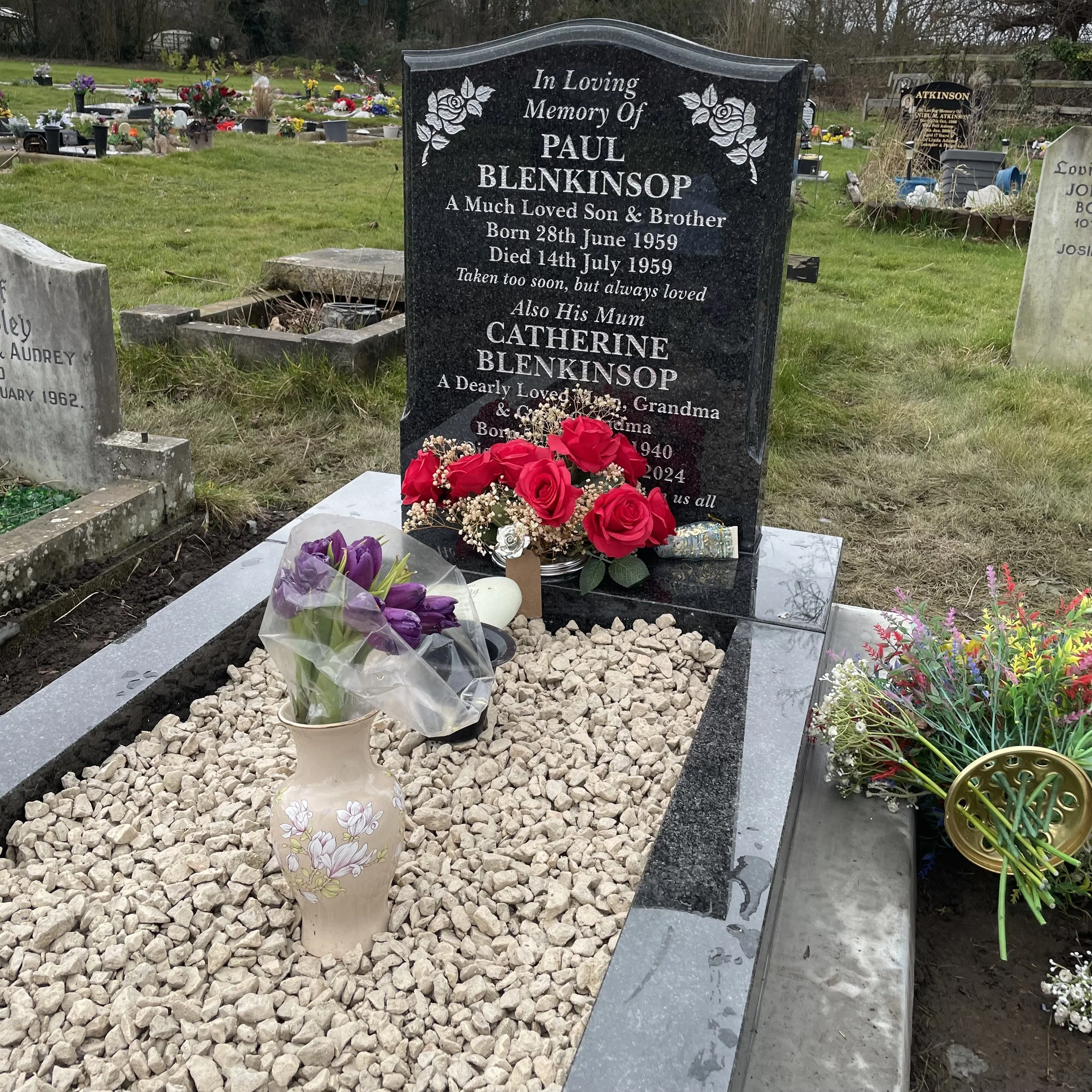 Gravestone for Paul Blenkinsop and Catherine Blenkinsop at a cemetery, decorated with red roses, purple tulips, and various flowers.