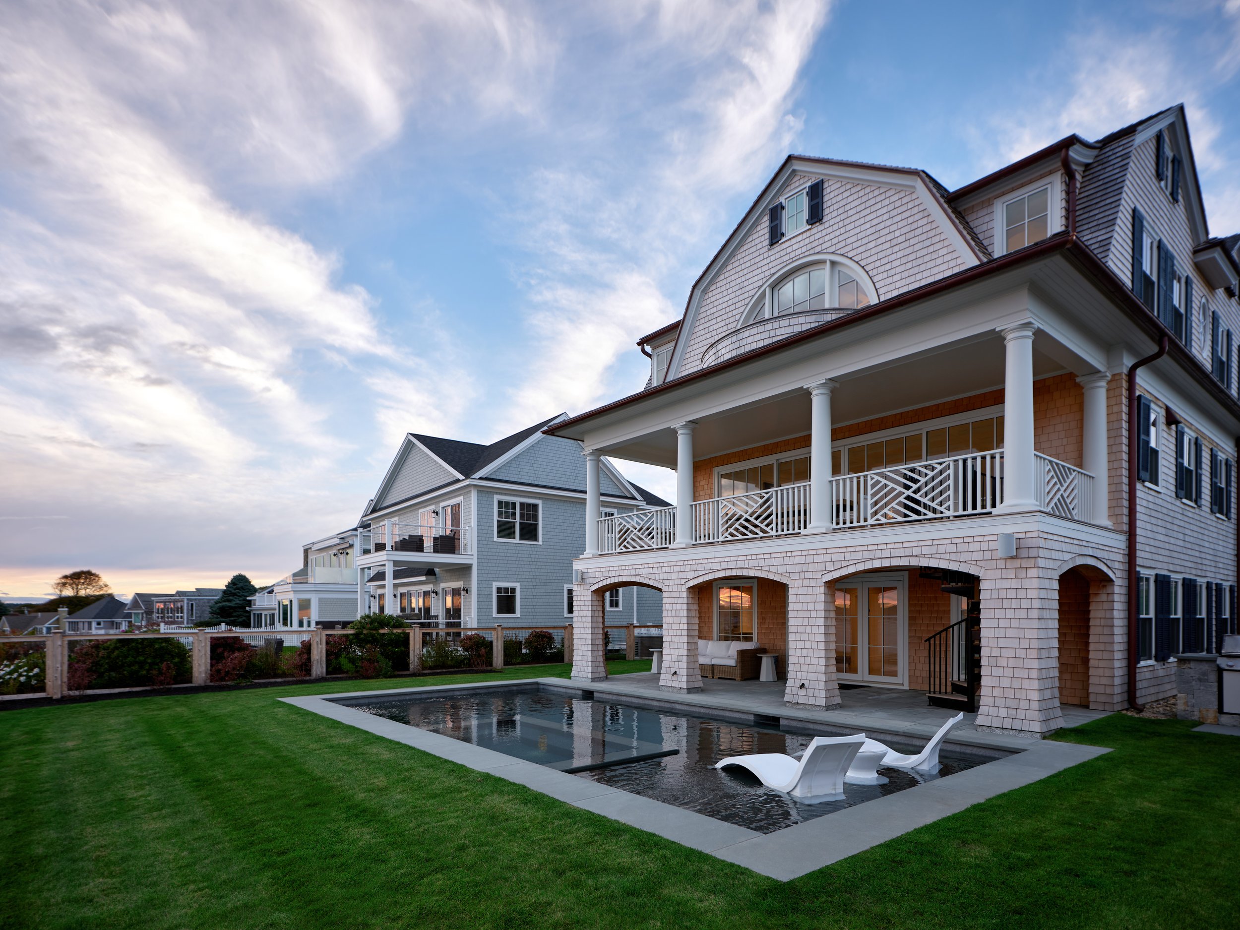 Exterior view of a large house with a pool and lounge chairs in the backyard, under a partly cloudy sky.