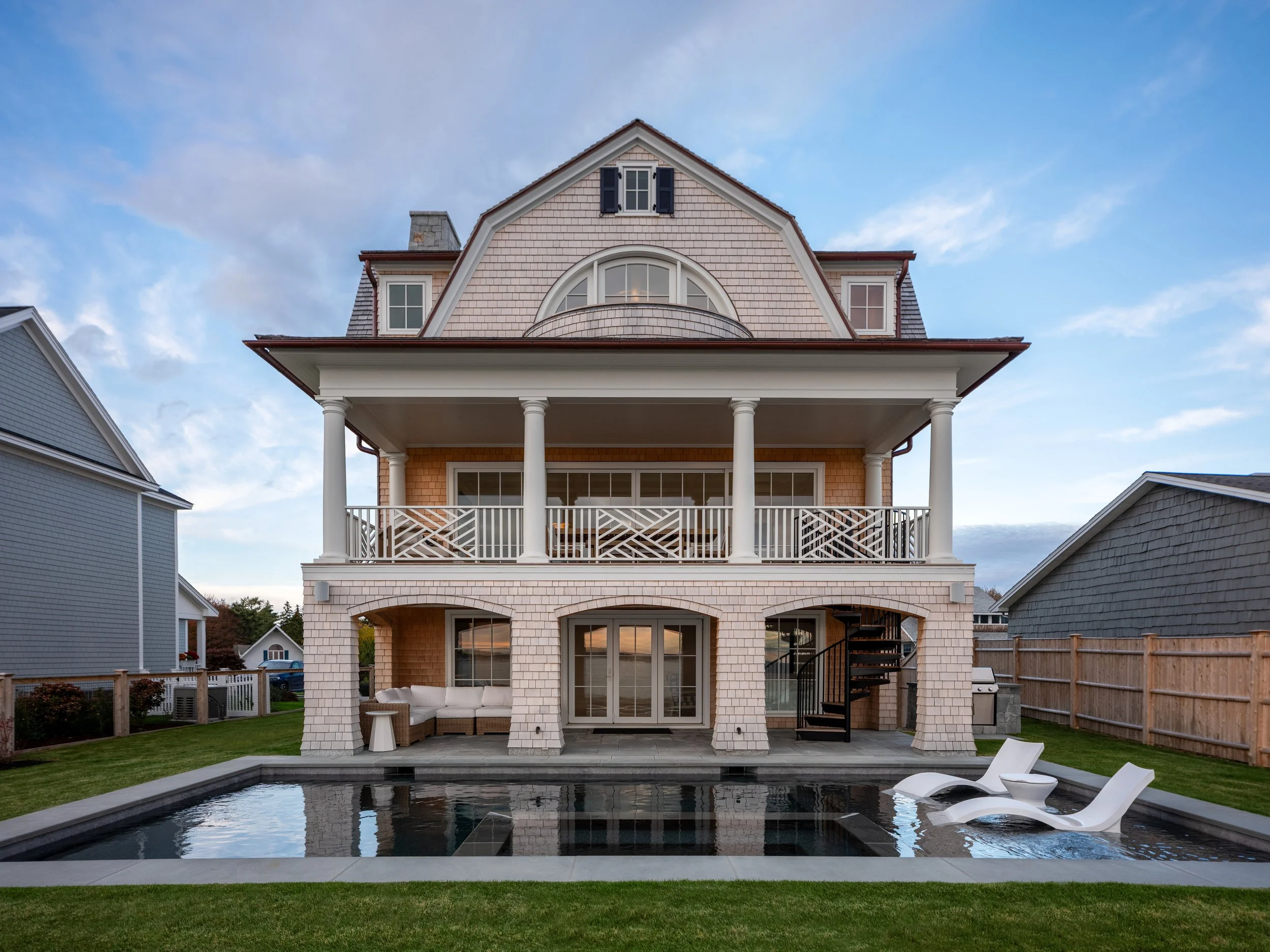 Three-story house with a balcony, cedar exterior, and a swimming pool in the backyard, under a blue sky with clouds.