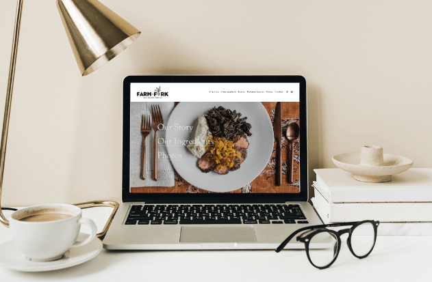 Laptop displaying a webpage with a plate of food, set on a beige desk next to a lamp, coffee cup, eyeglasses, and a stack of books.