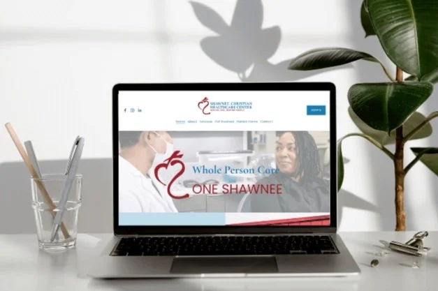 Laptop displaying a healthcare website in a bright setting with plants and a glass containing pencils beside it.