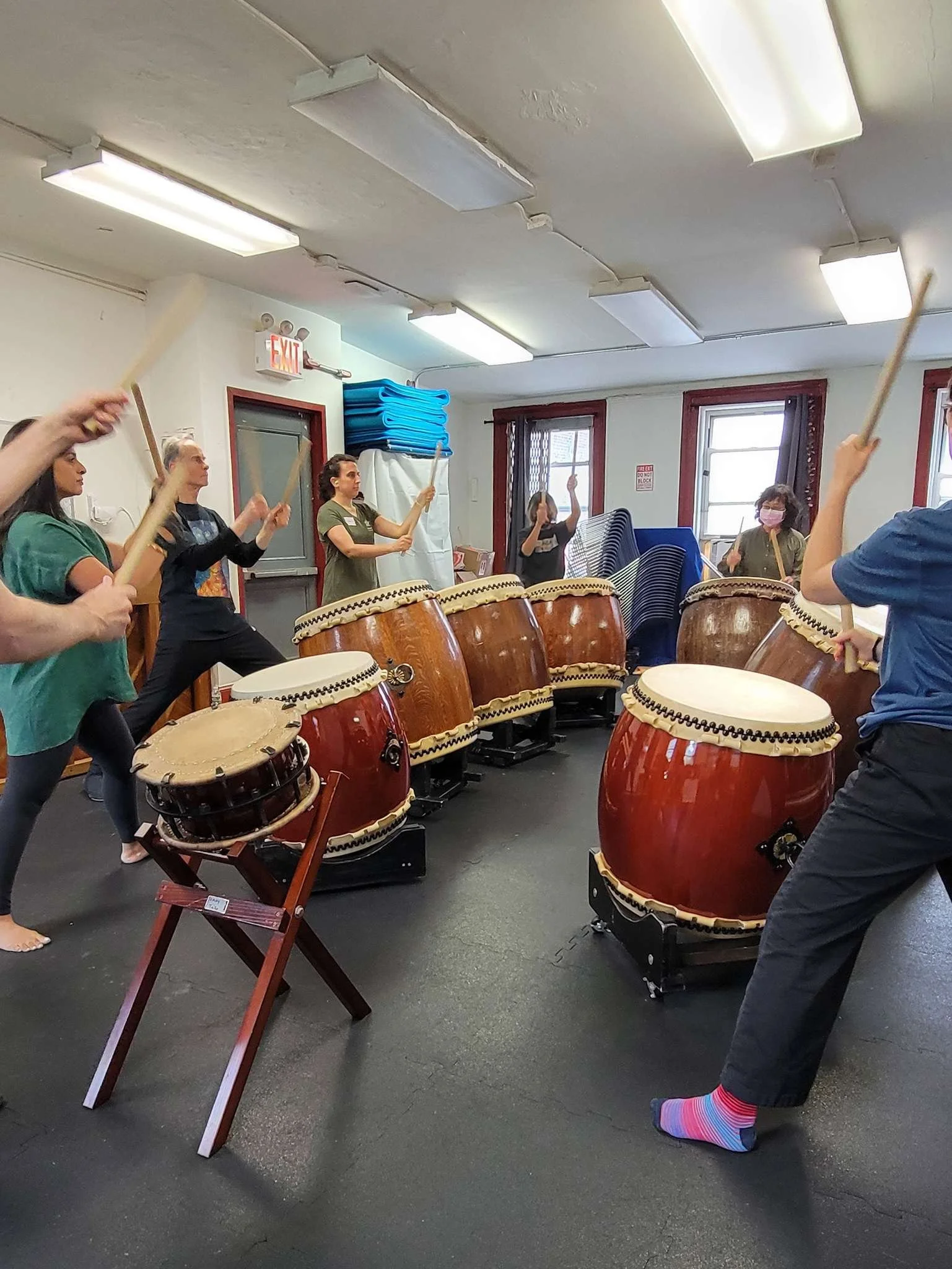 Group of people practicing taiko drumming in a room with drums and windows.