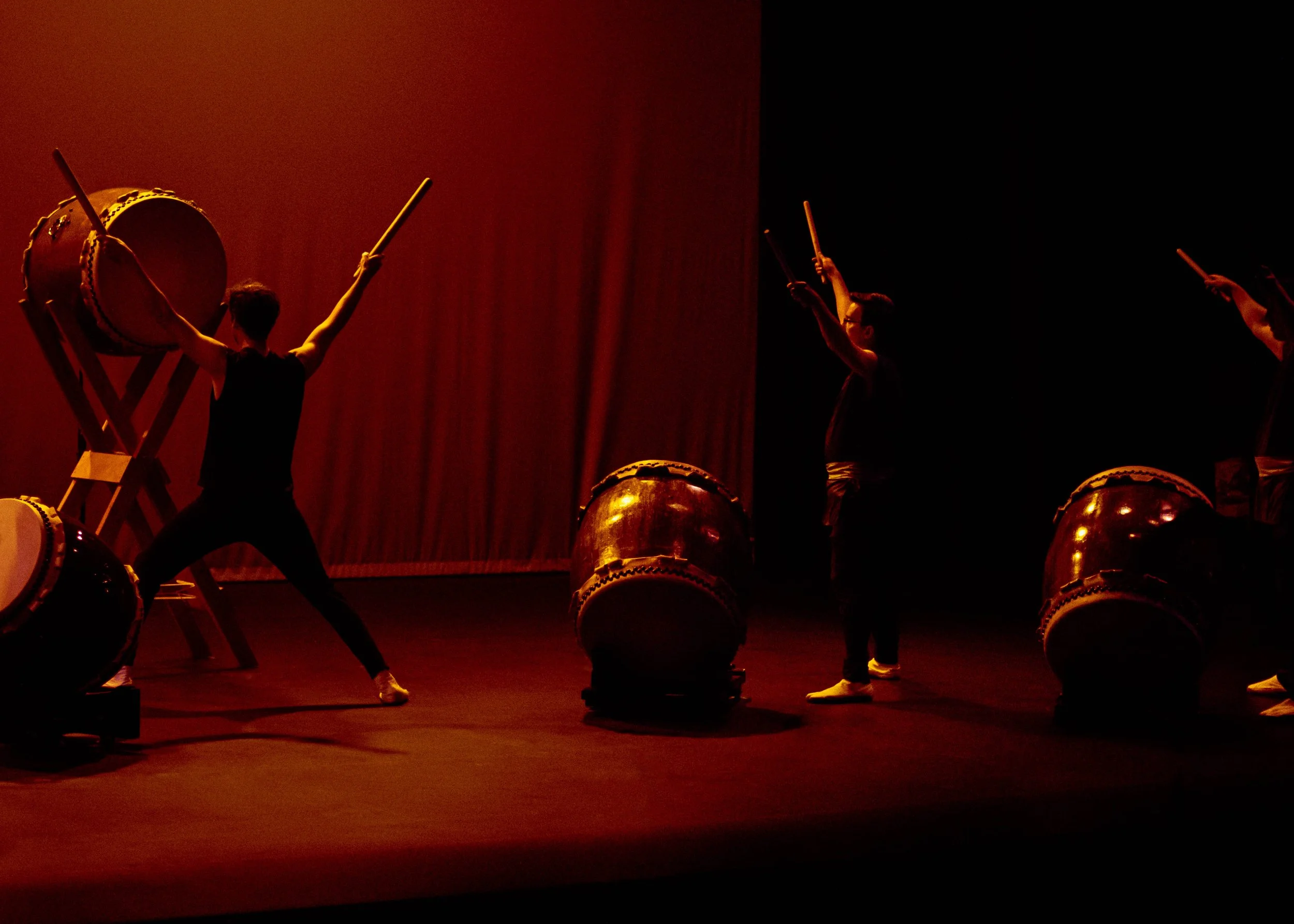 Group of performers dressed in black practicing Japanese taiko drumming on stage with dim lighting.