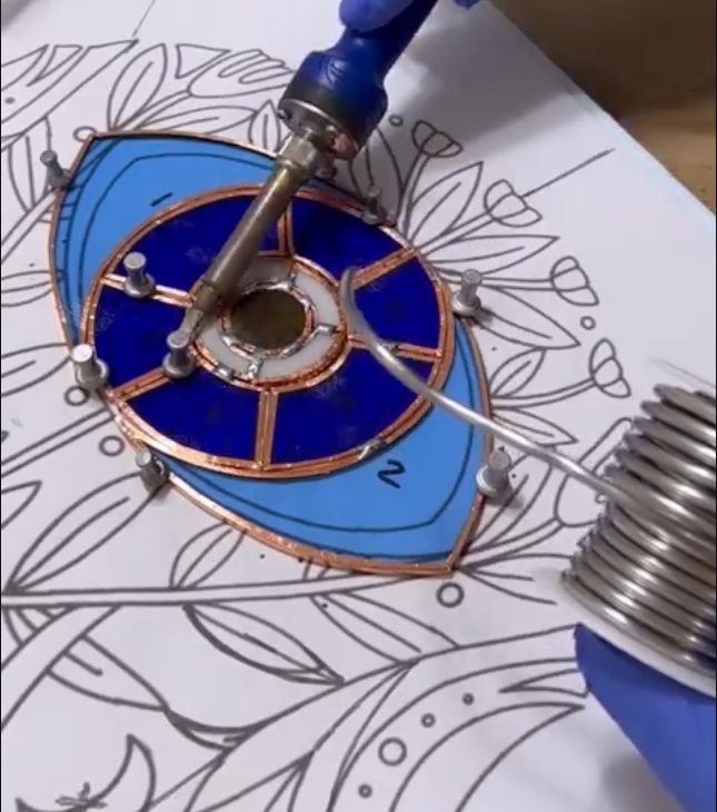 An in-progress stained glass art piece of a warding evil eye, showing the handiwork proces of creating stained glass artwork.