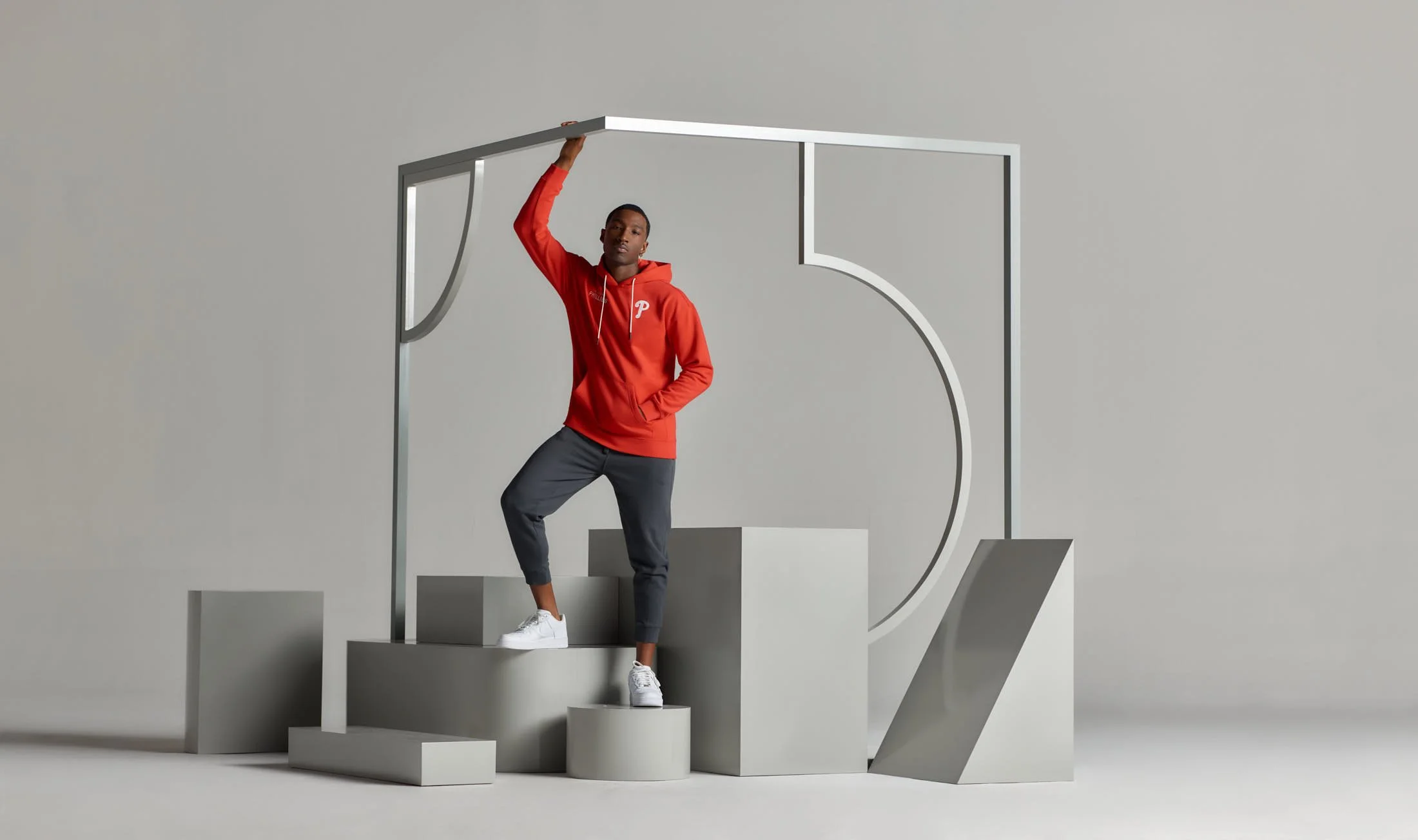 Person in red hoodie and black pants posing on geometric shapes