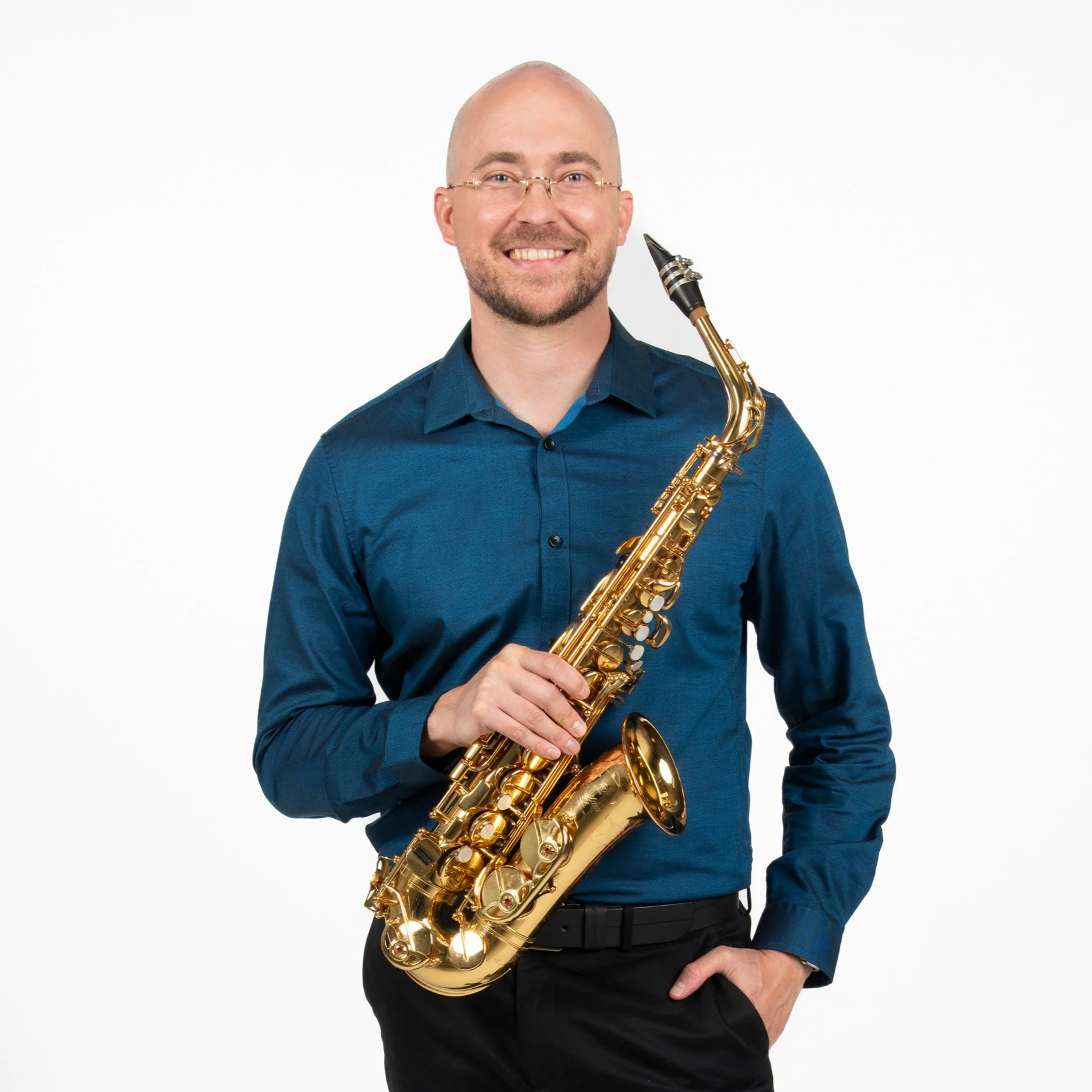 A man with glasses, a beard, and a bald head holding a golden saxophone, smiling, standing against a white background.