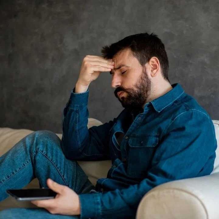Man sitting on a couch looking distressed by intrusive thoughts.